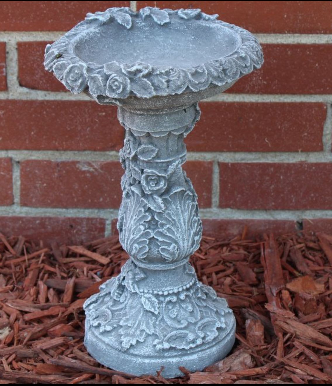 Decorative gray stone pedestal birdbath with floral reliefs