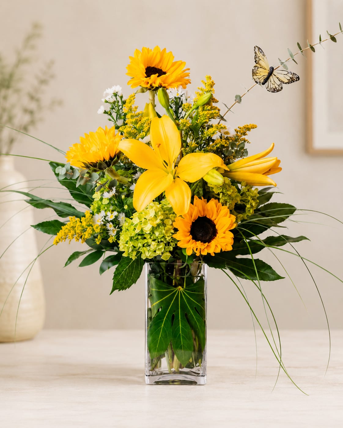 Yellow lilies and sunflowers in a clear glass vase with a butterfly pick