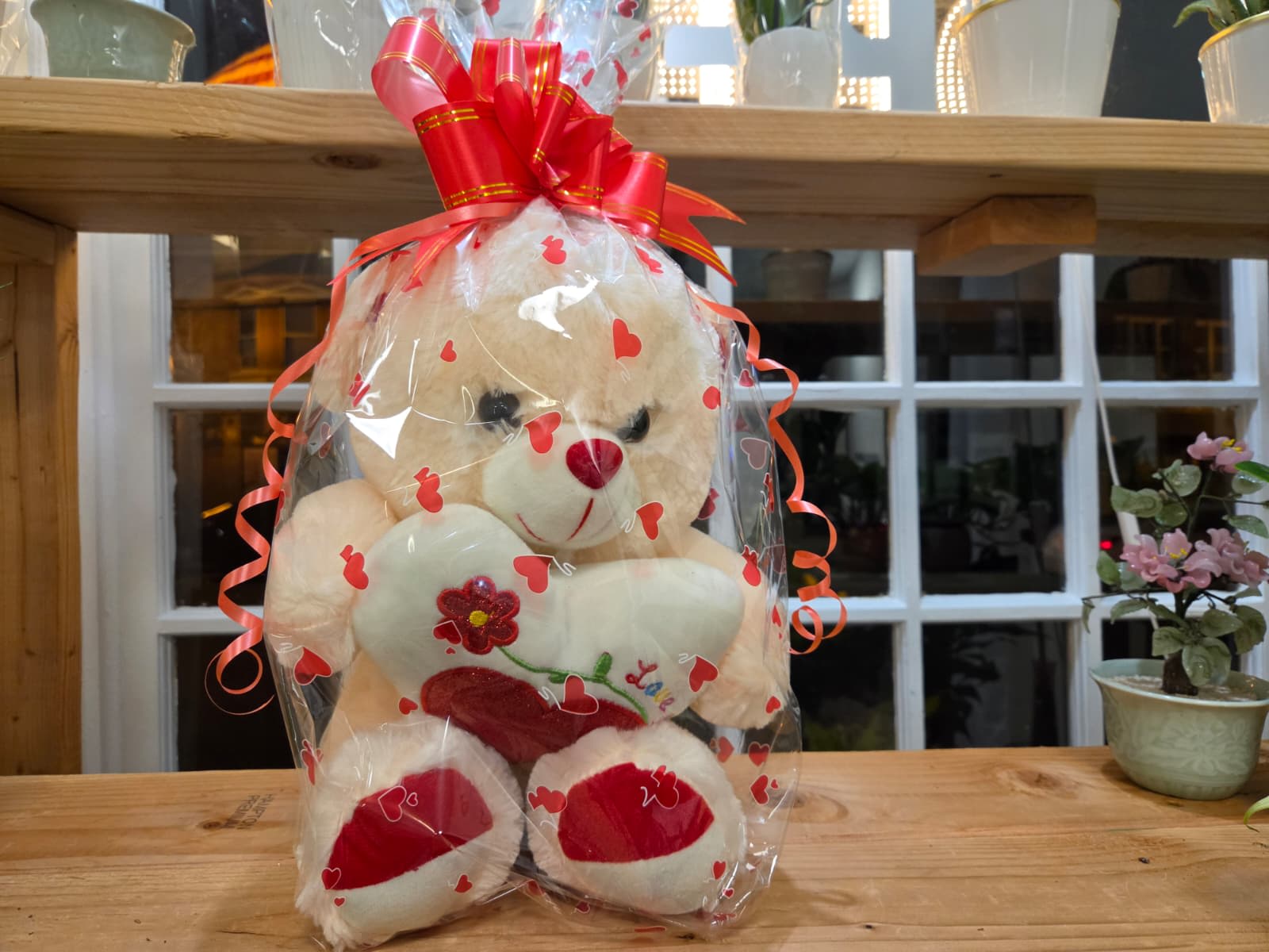 Cream teddy bear in heart-print cellophane with a red bow