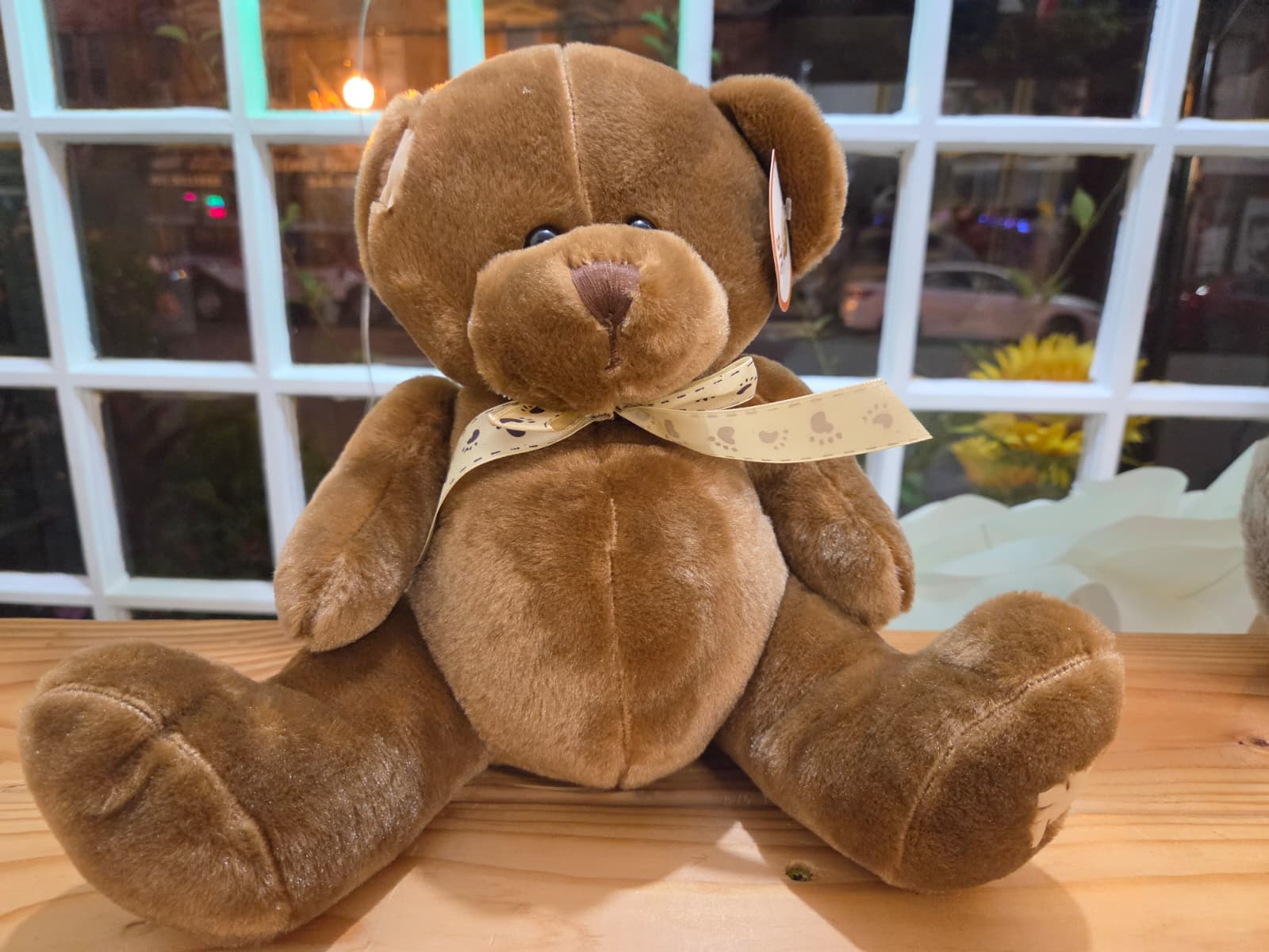 Brown teddy bear with a ribbon sitting on a wooden surface