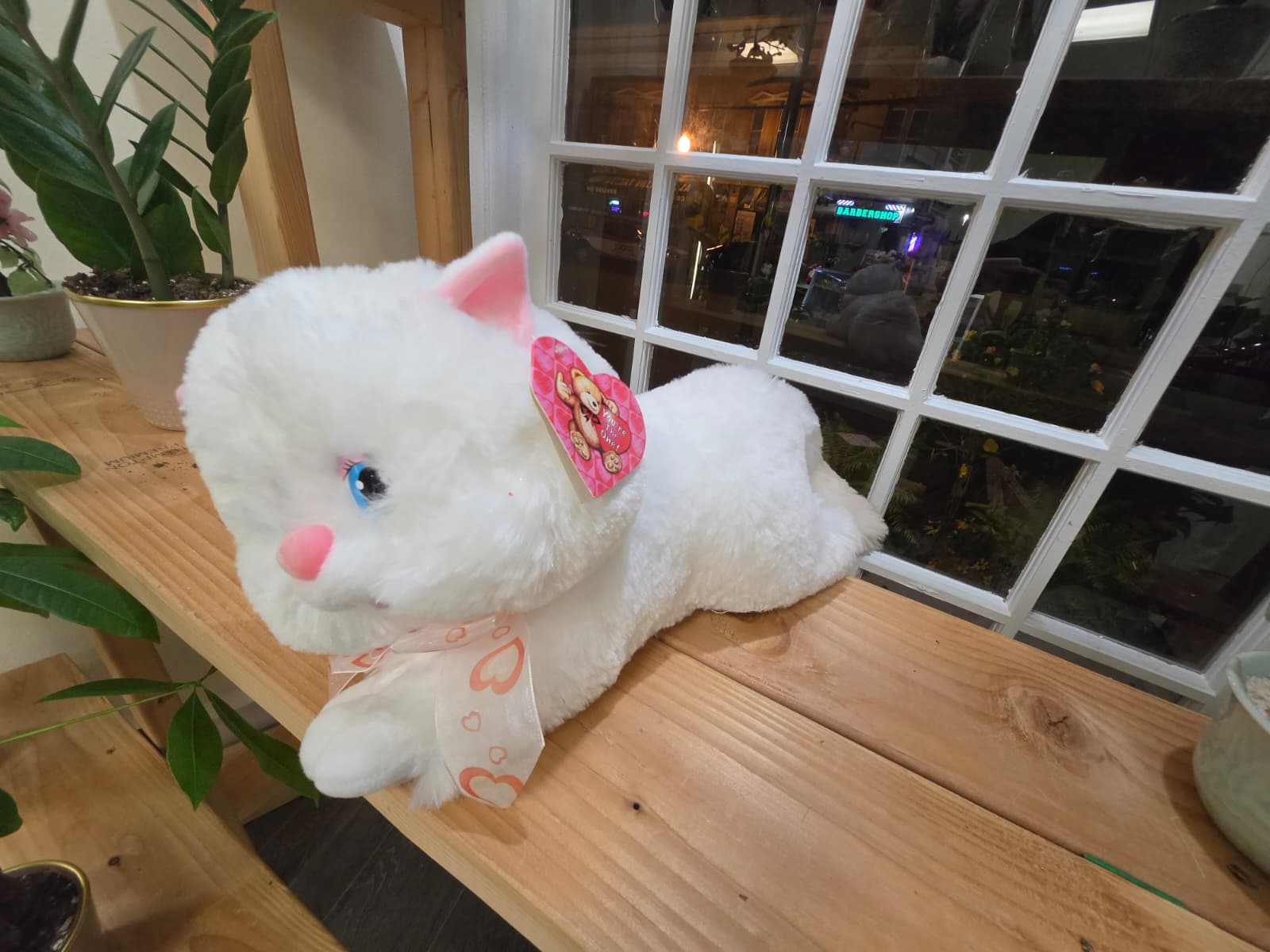 White plush cat with pink ears and a ribbon on a wooden shelf