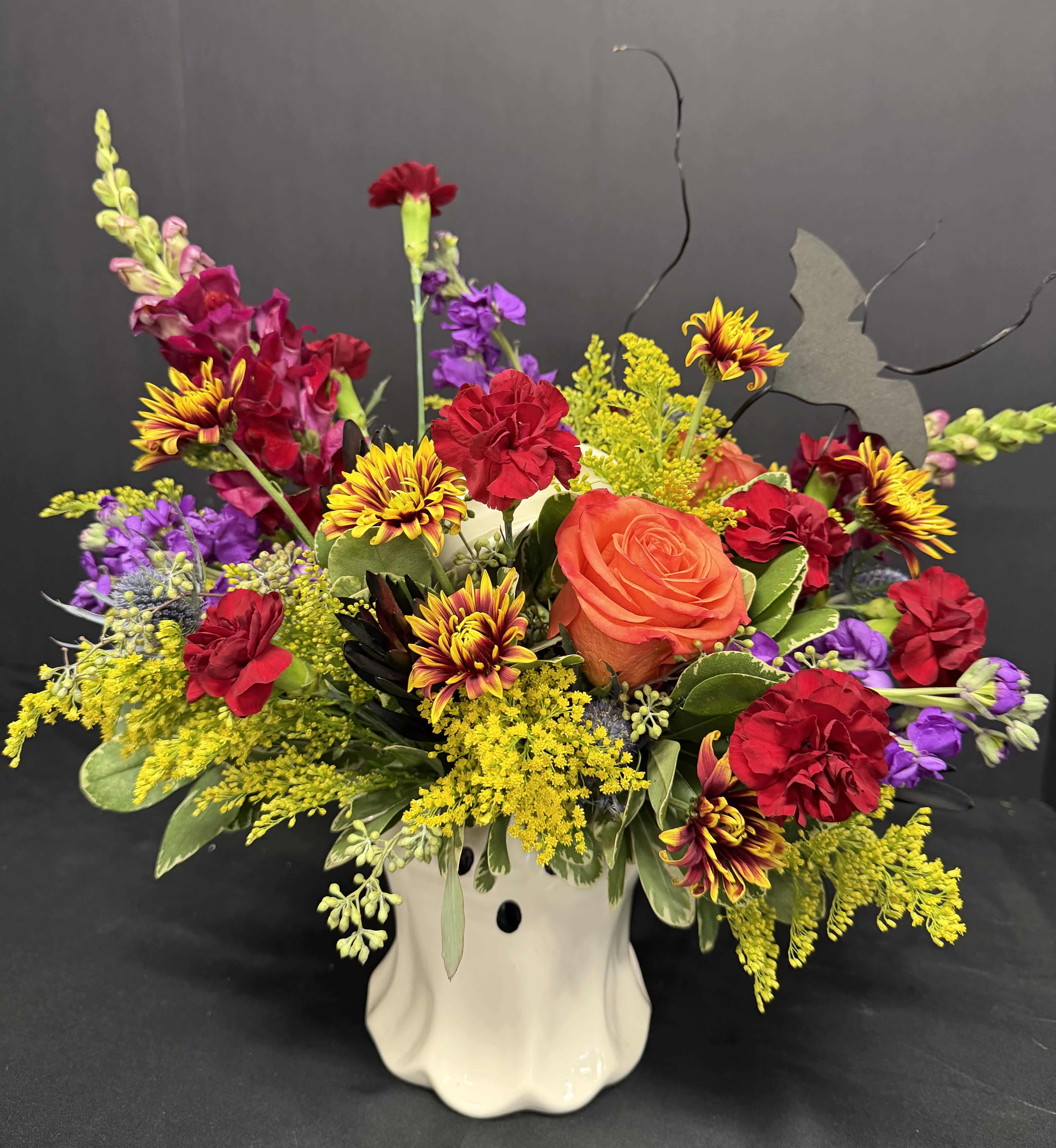 Colorful floral arrangement in a white ceramic vase with roses, carnations, and mixed blooms