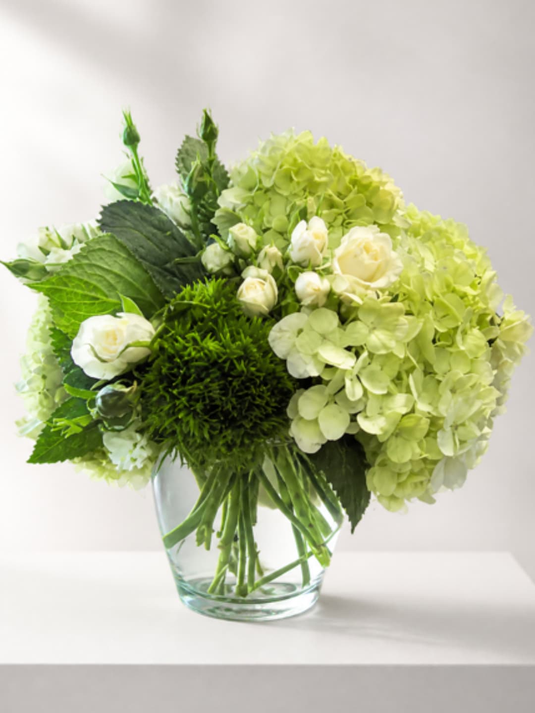 Green hydrangeas and white roses in a clear glass vase