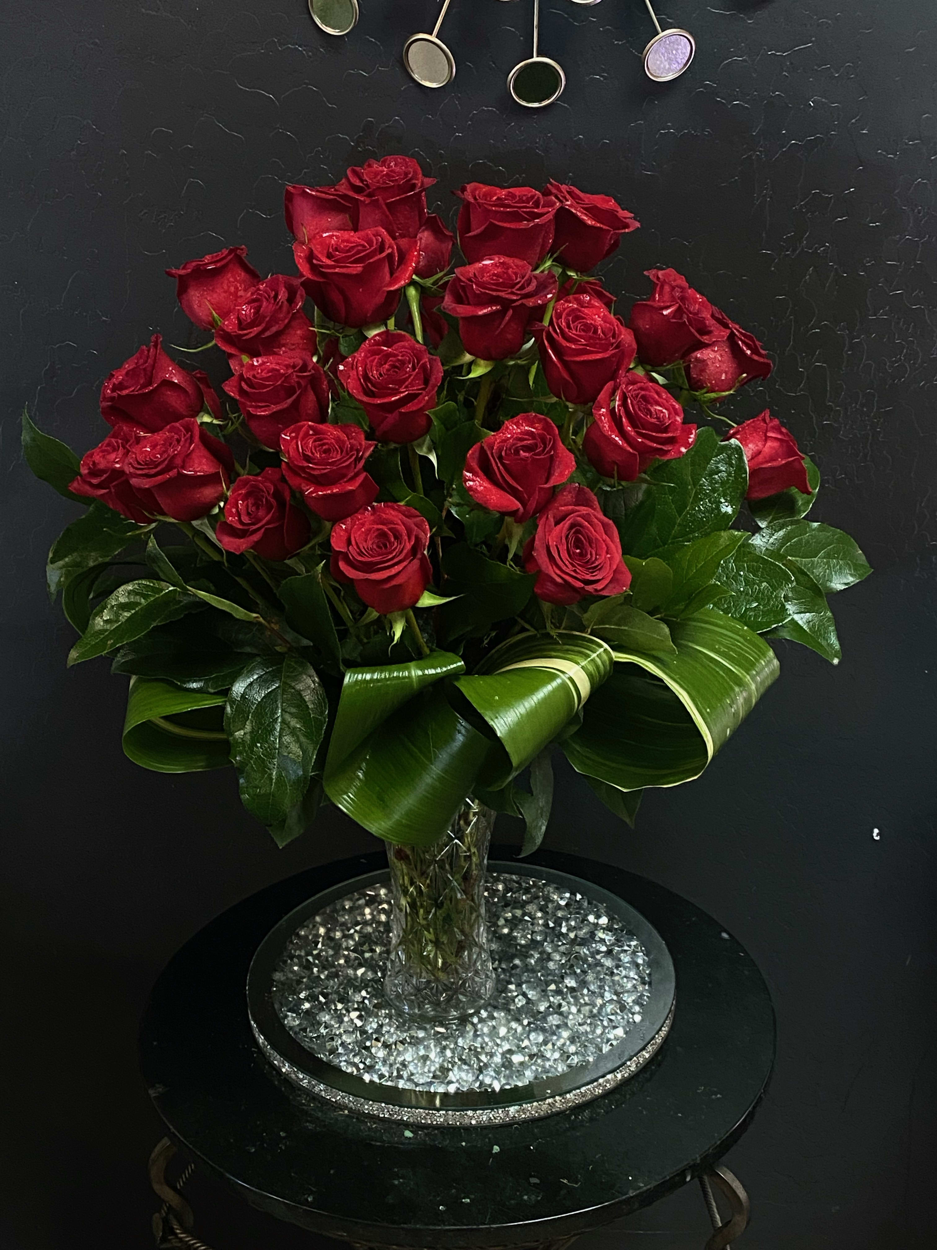 Red roses arranged in a clear vase with glossy leaves