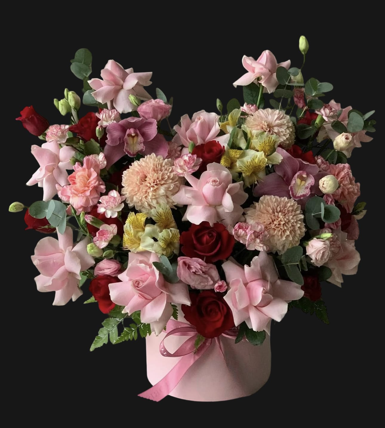 Pink and red mixed flower arrangement in a round box