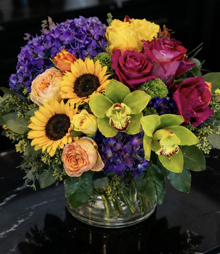 Colorful bouquet with roses, sunflowers, orchids, and hydrangeas in a glass vase