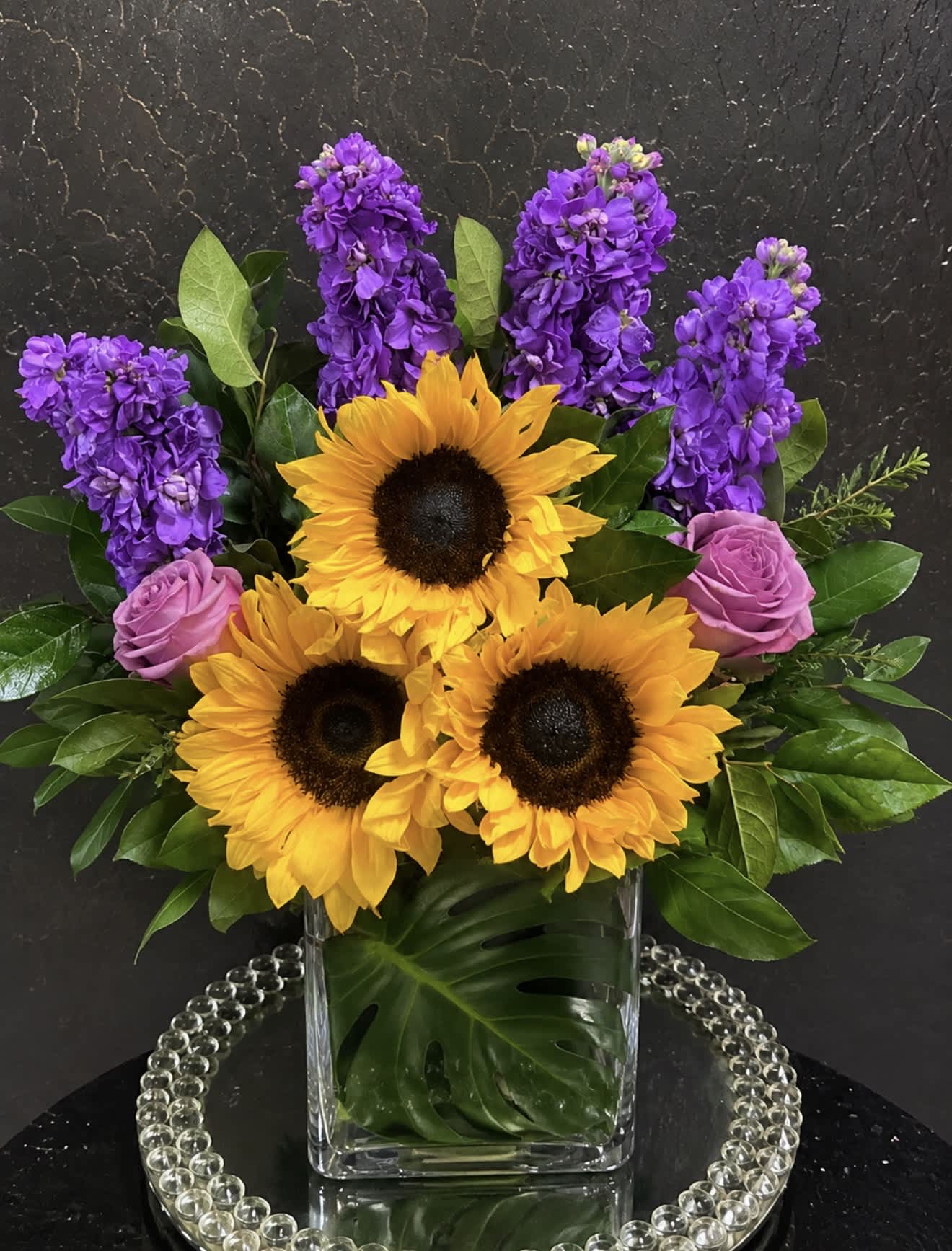 Sunflowers, purple stock, and pink roses in a clear glass vase