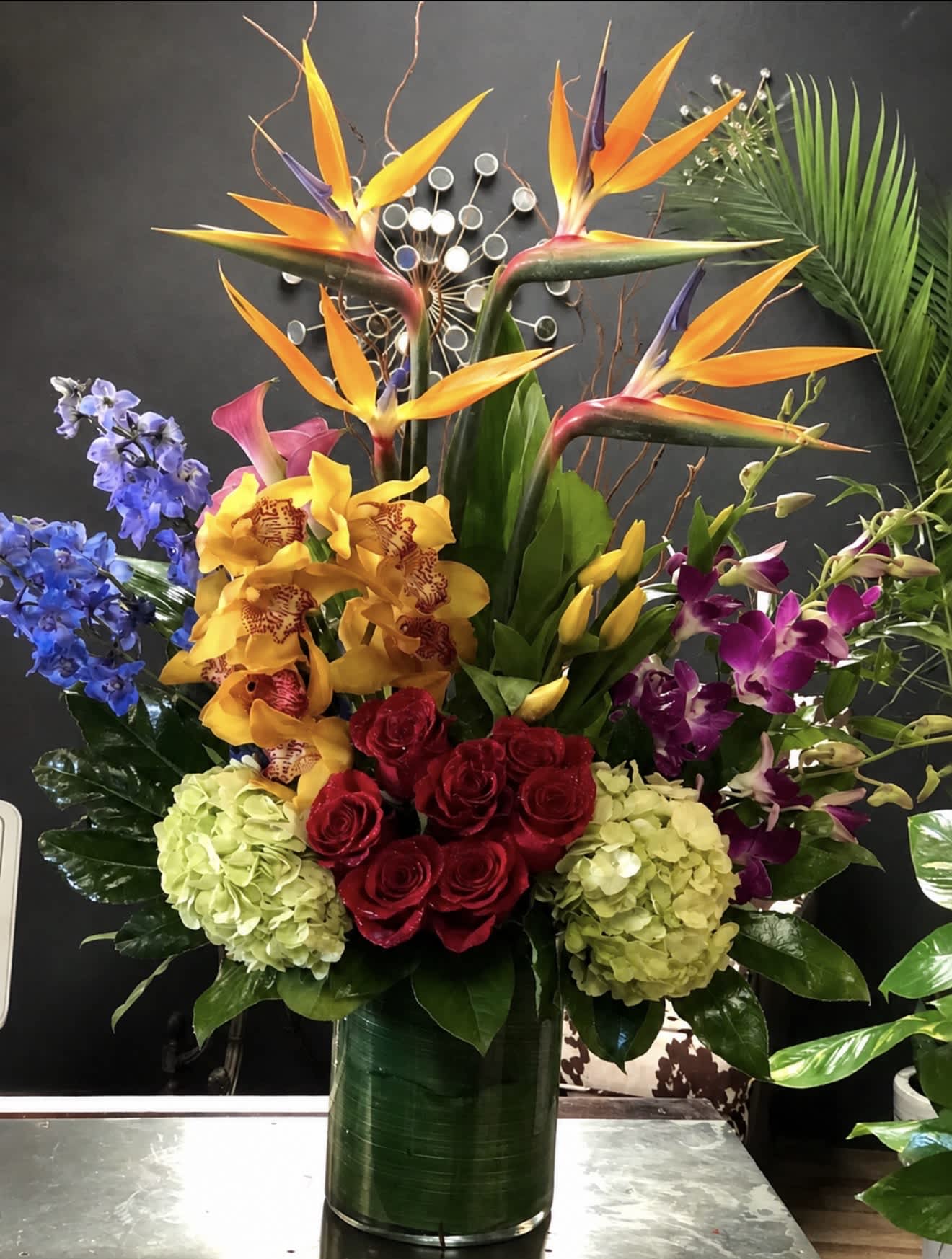 Tropical bouquet with bird of paradise, orchids, roses, and hydrangeas in a tall vase.