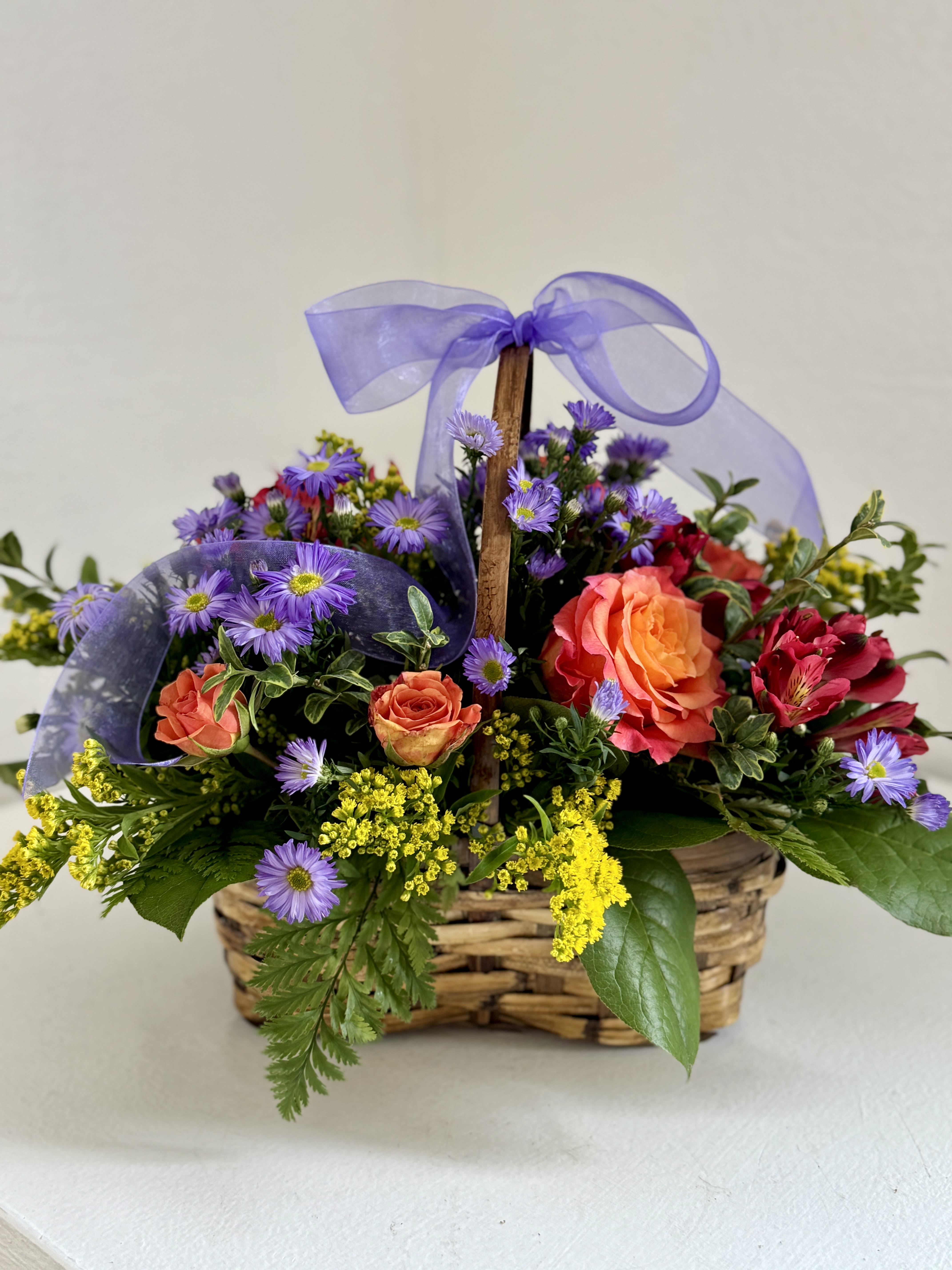 Basket of orange roses and purple daisies with a lavender ribbon