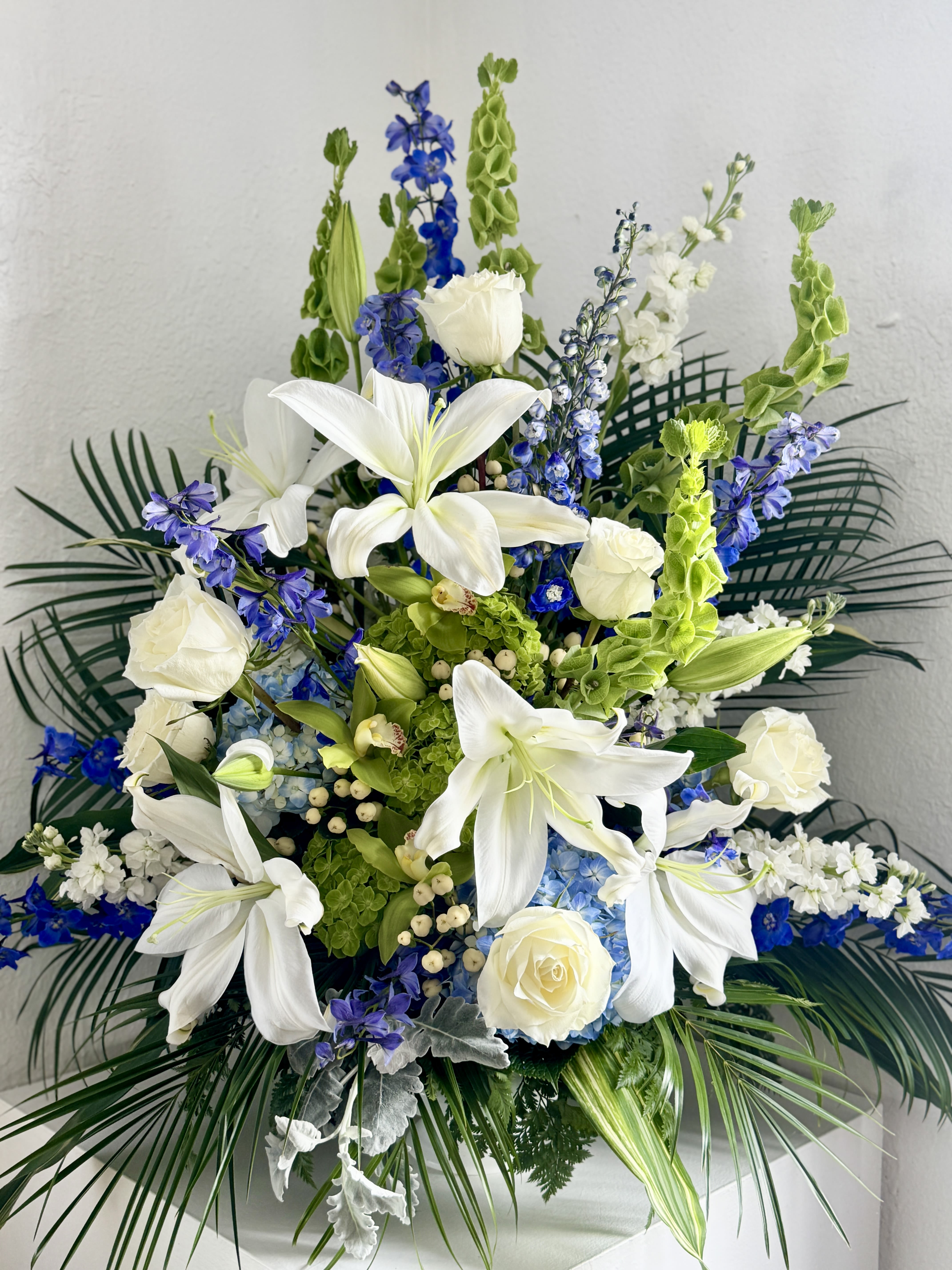 Celestial Rest - A single-faced urn arrangement that evokes a peaceful, heavenly rest with white, green, and pops of blue color throughout. 