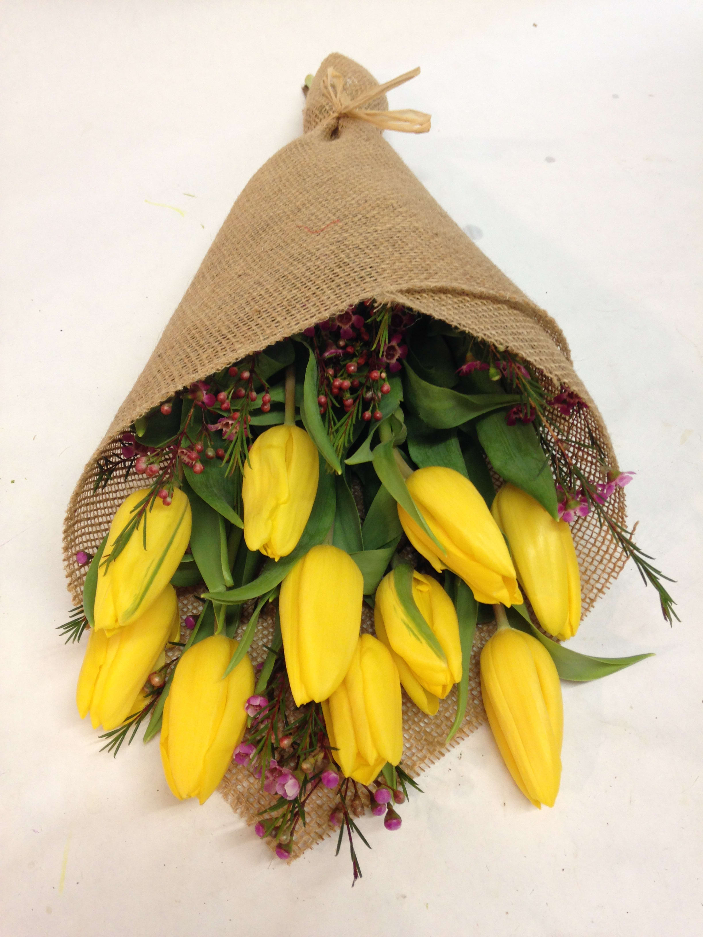 Bundle of yellow tulips wrapped in burlap with small purple flowers