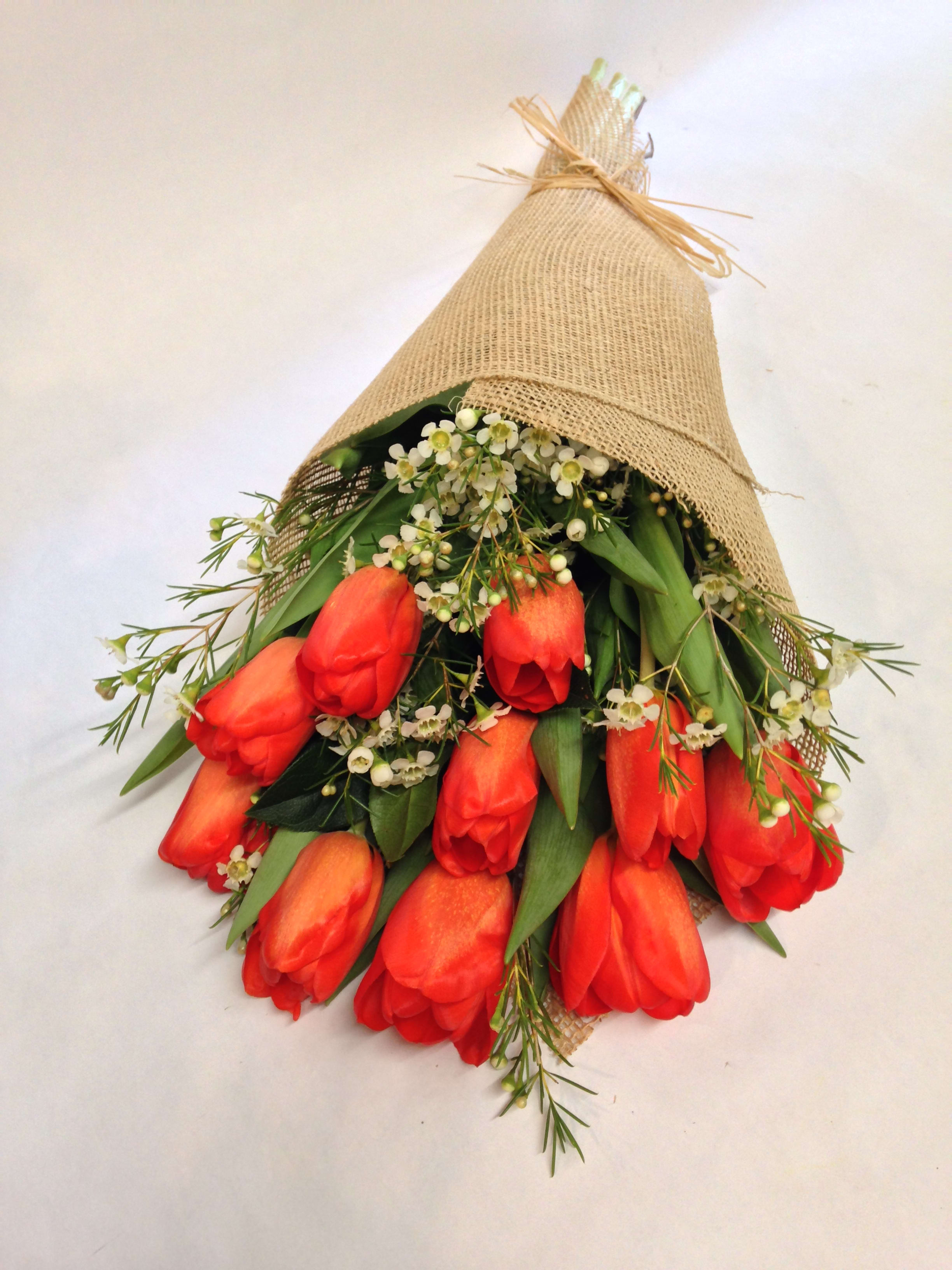 Bouquet of red tulips wrapped in burlap with small white filler flowers