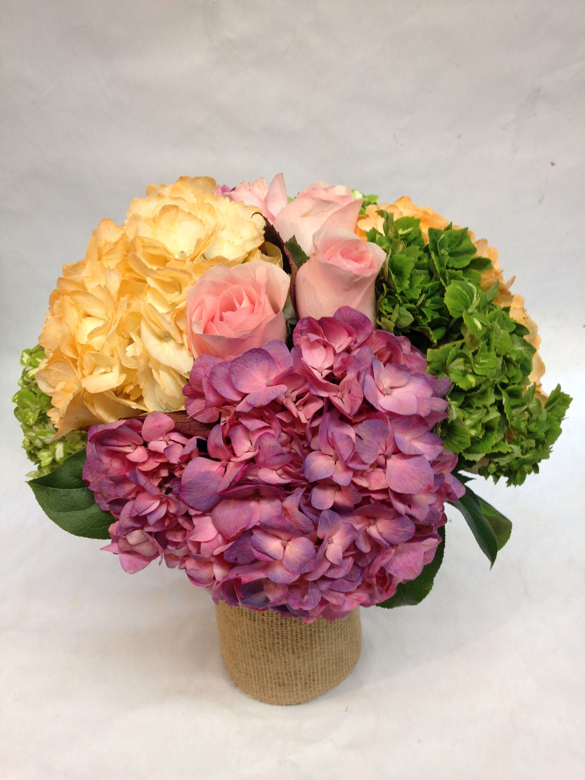 Bouquet of pink roses and hydrangeas in a burlap-wrapped container
