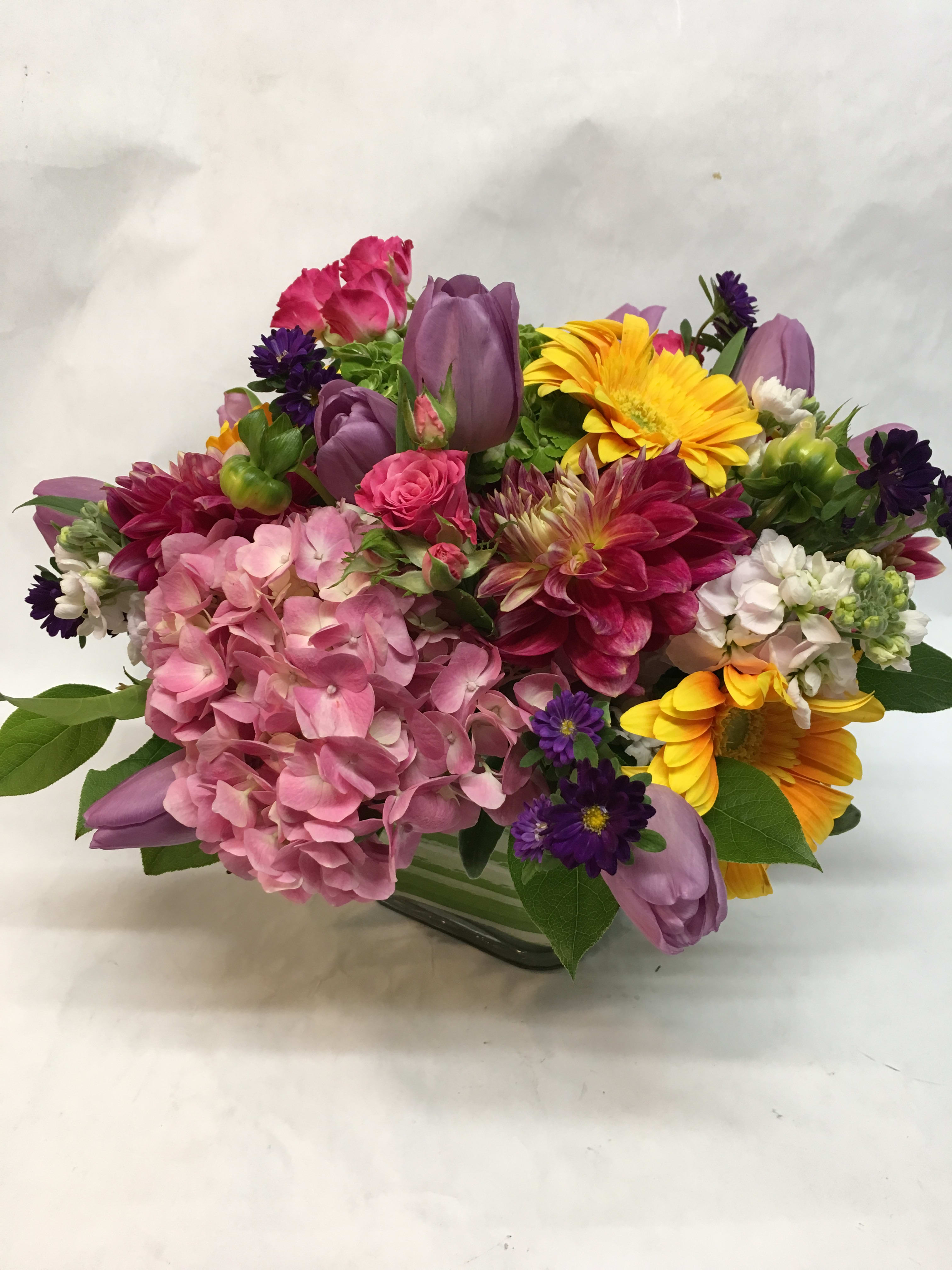 Mixed bouquet with pink hydrangea, purple tulips, and yellow daisies in a glass vase