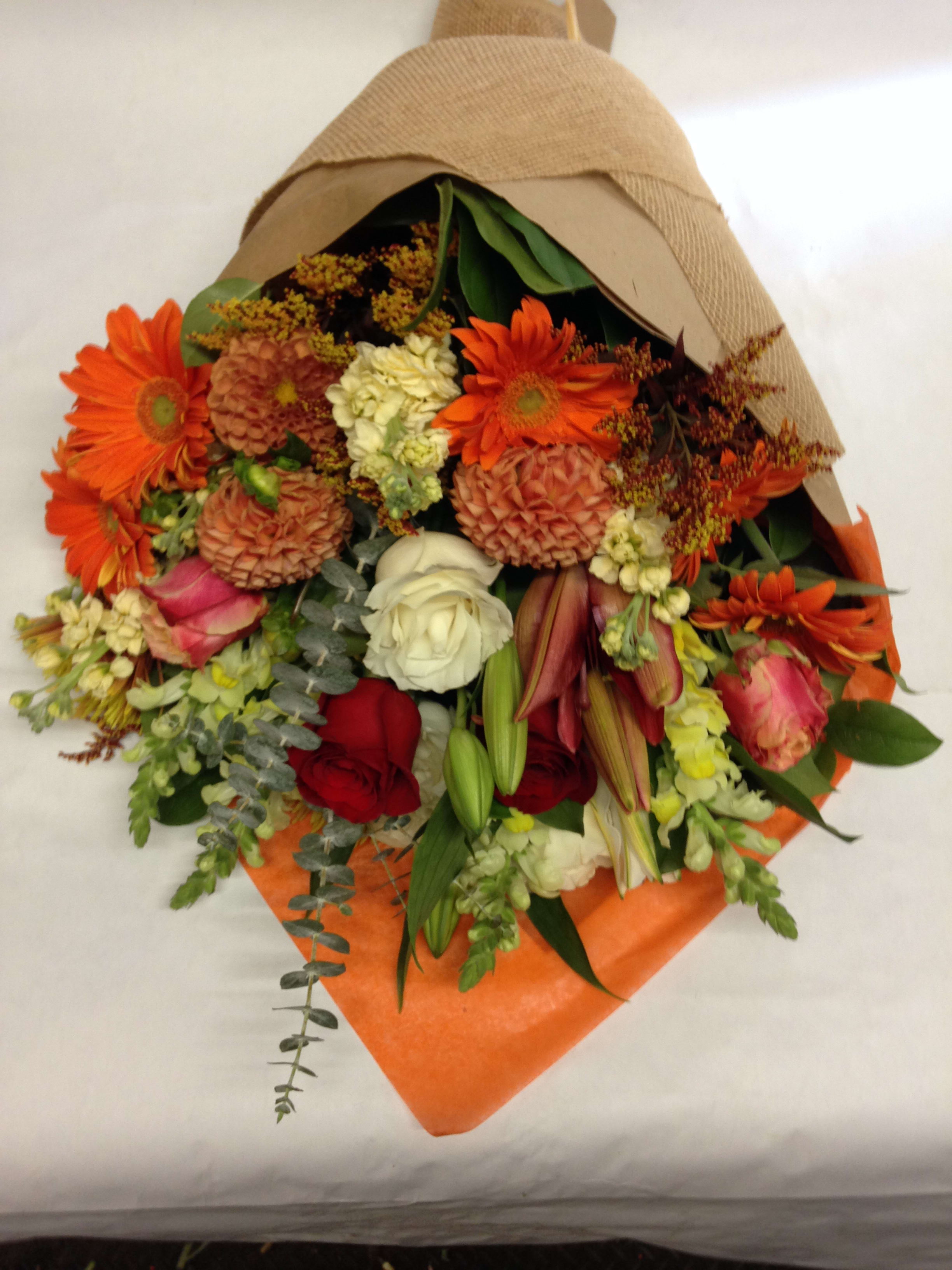 Mixed bouquet with orange daisies, roses, and lilies wrapped in brown paper