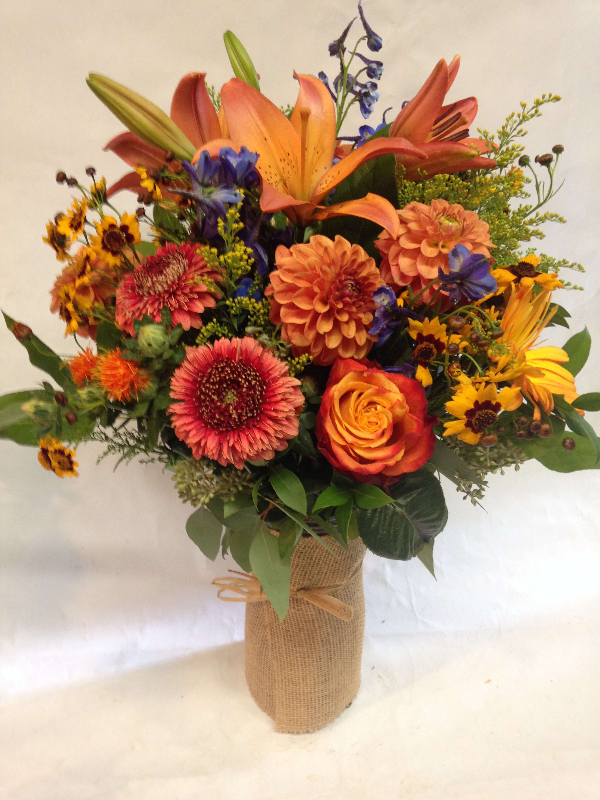 Colorful bouquet of lilies, roses, and daisies in a burlap-wrapped vase