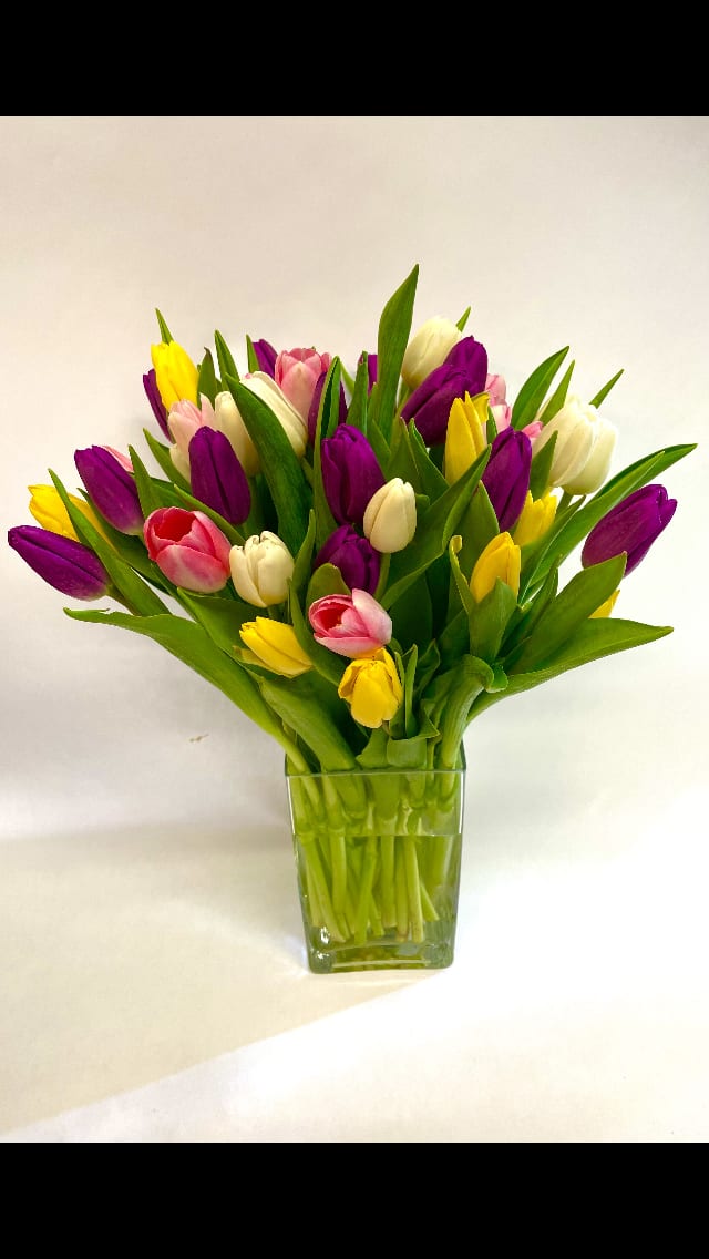 Arrangement of purple, yellow, white, and pink tulips in a clear square glass vase
