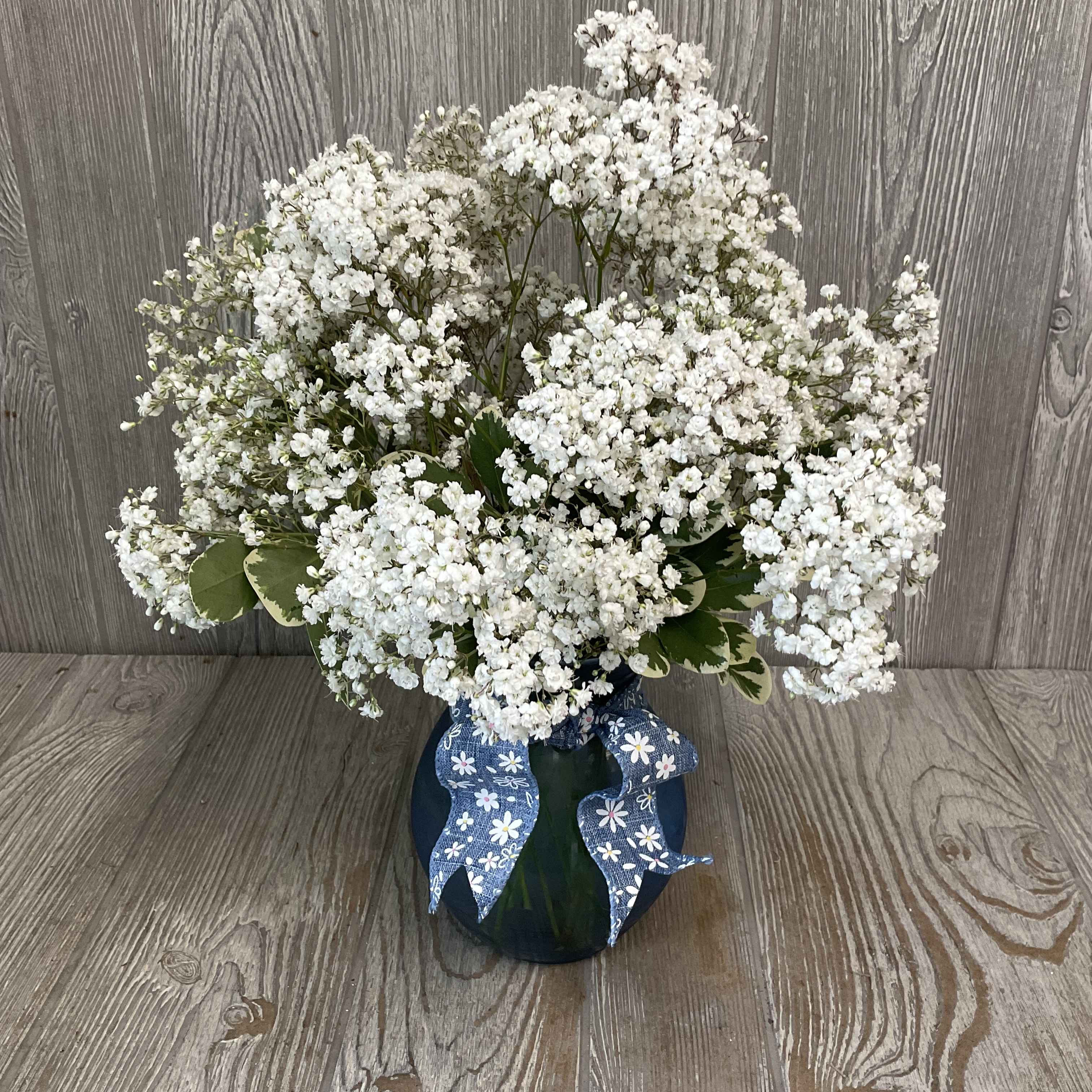 White baby's breath arrangement in a dark vase with a blue ribbon