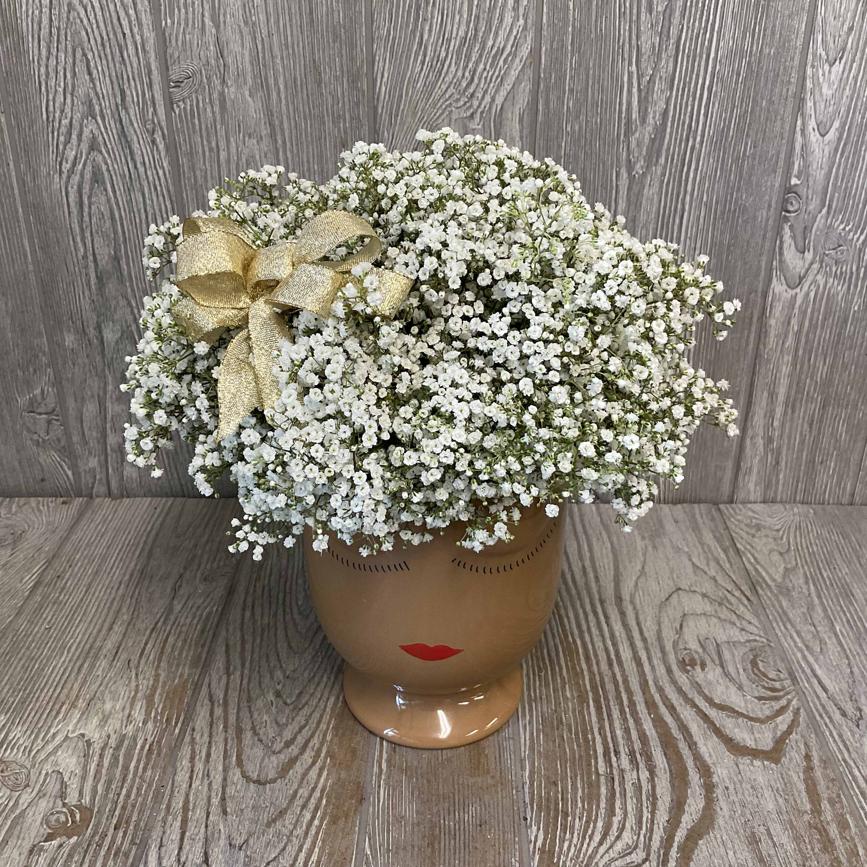 White baby's breath arrangement in a face-shaped ceramic vase with a gold bow