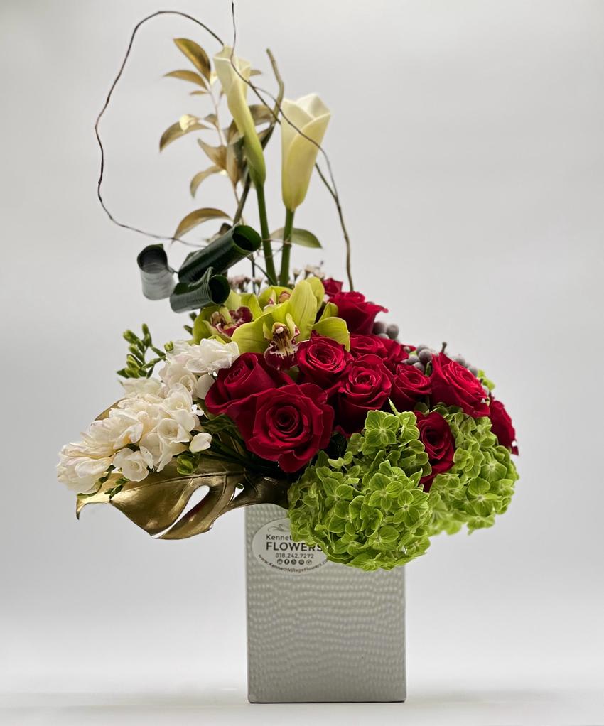 Sky High - This arrangement is designed to make a bold and dramatic statement, with tall stems of the calla lilies raising from red roses, hydrangeas and orchids, creating a dramatic vertical display. The red roses in the arrangement add a warm and passionate energy, while the calla lilies bring a touch of sophistication and elegance. The scrambled green leaves serve as a beautiful contrast to the flowers, adding texture and depth to the overall design.  The name "Sky High" speaks to the eye-catching display of the arrangement, which can be used to decorate a room or to make a bold statement in a public space. It is arranged in a contemporary rectangular container to make a lasting impression and bring joy to whoever sees it. With its vibrant color combination and striking design, Sky High is a perfect choice for special occasions and celebrations, or as a gift for someone you care about.