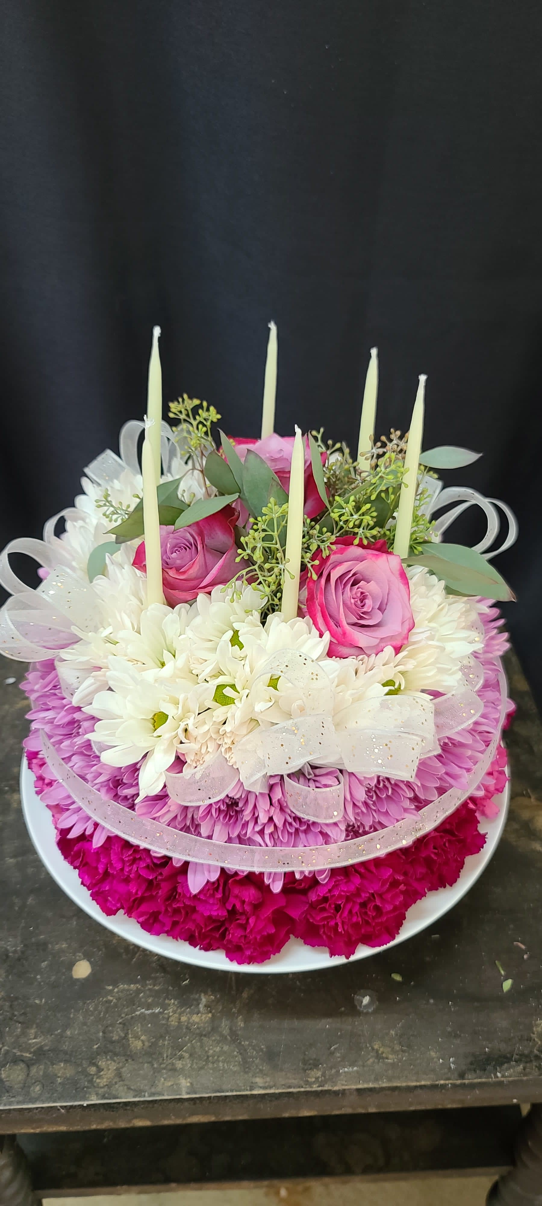 Round floral arrangement with pink roses, white daisies, and tall candles