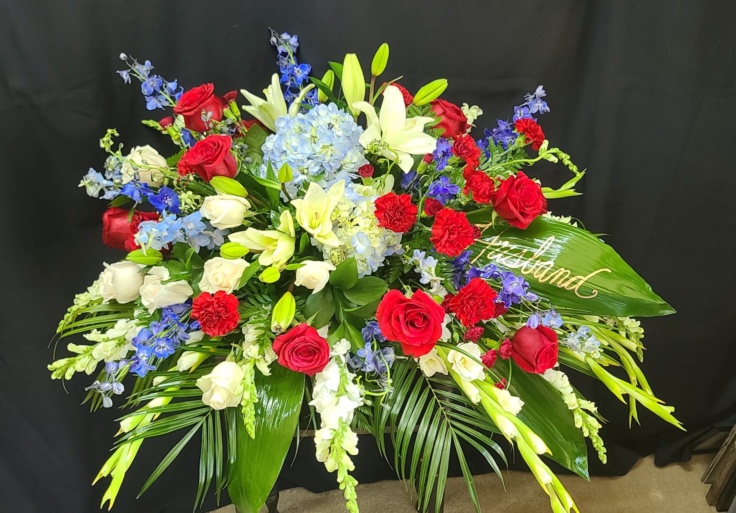 Large floral spray with red and white roses, lilies, and blue flowers