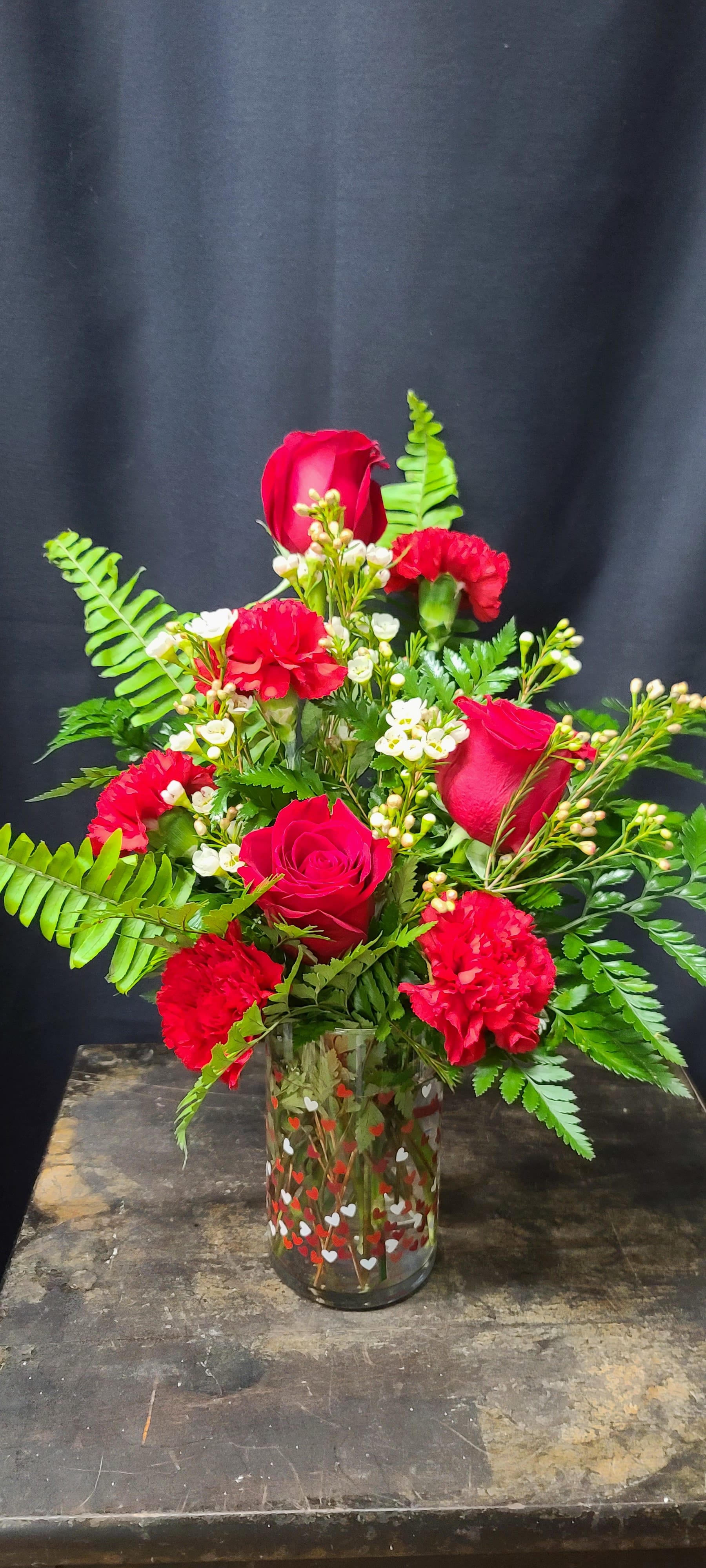 Red roses and carnations in a clear glass vase with fern foliage
