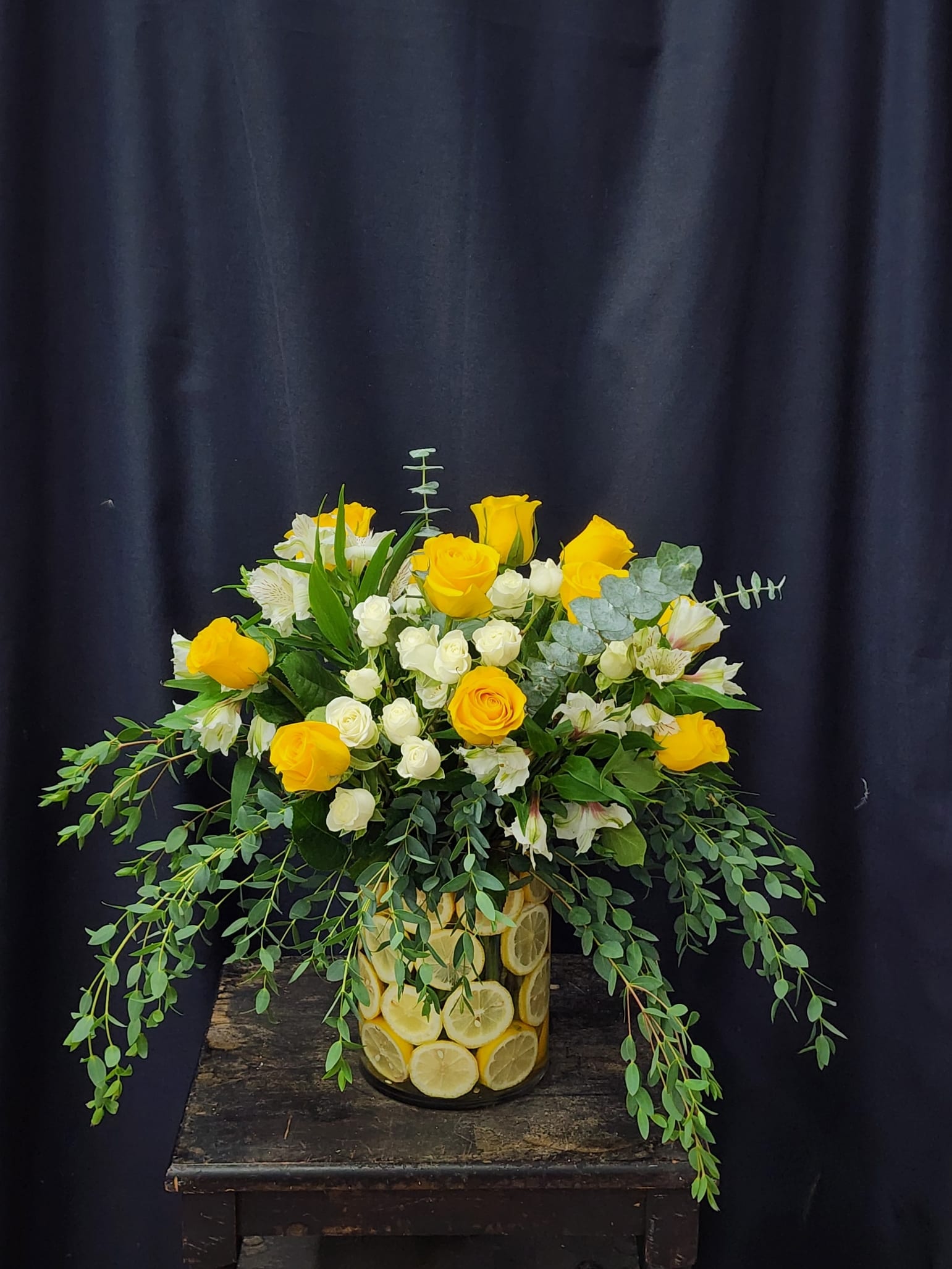 Yellow roses and white spray roses in a lemon-filled glass vase