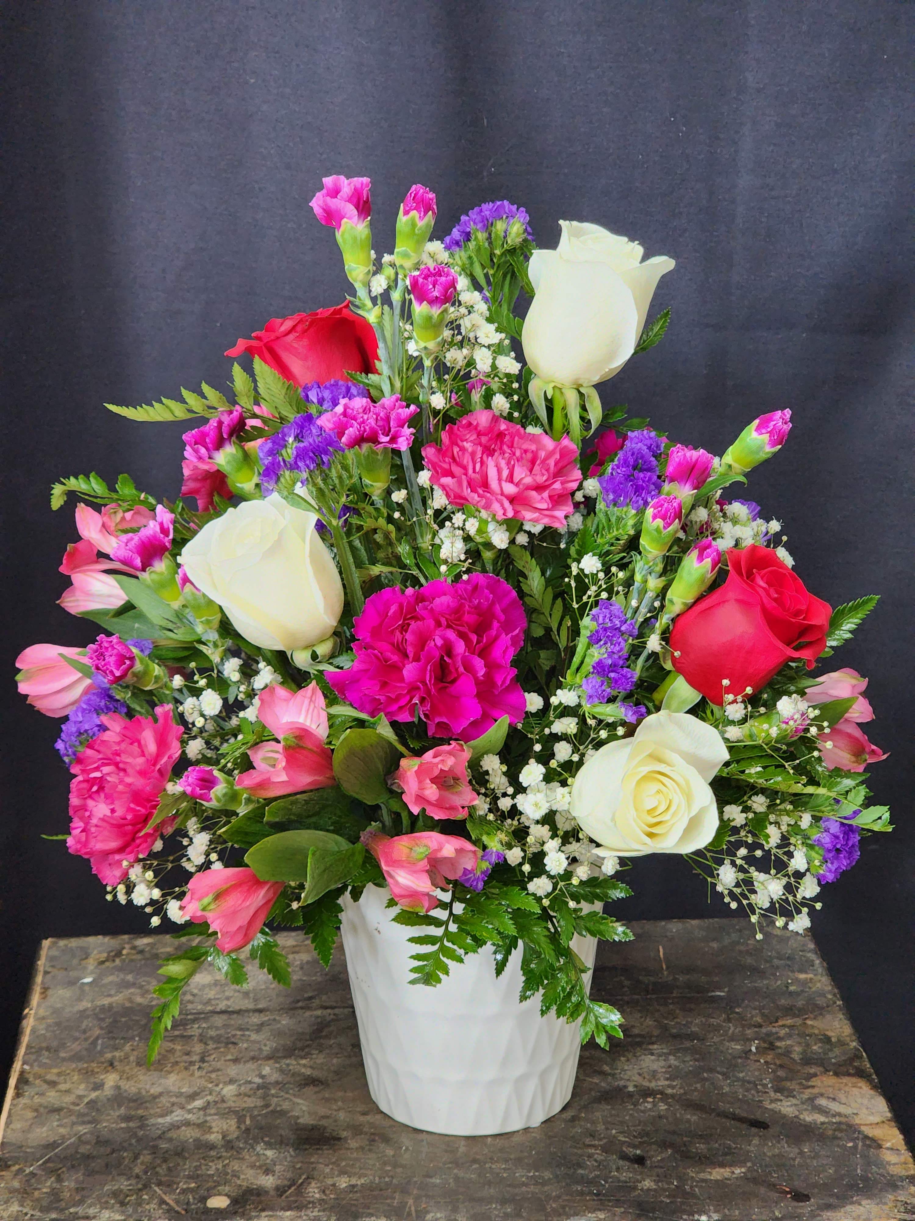Mixed bouquet of roses, carnations, and purple filler in a white vase