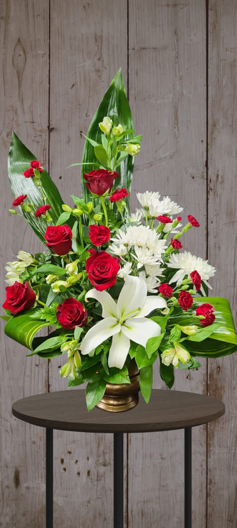 Modern Funeral Urn Red &amp; White - A modern twist on a traditional favorite. Just as elegant as always but with a modern flare, red roses, a white lily, alstroemeria, and red mini carnations are accented with ti leaves 