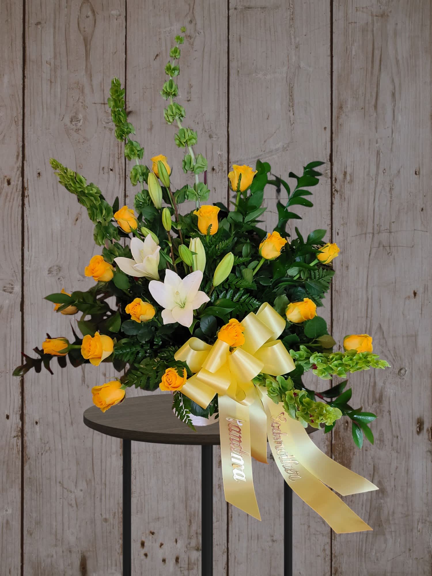 Yellow roses and white lilies in a vase with a yellow ribbon
