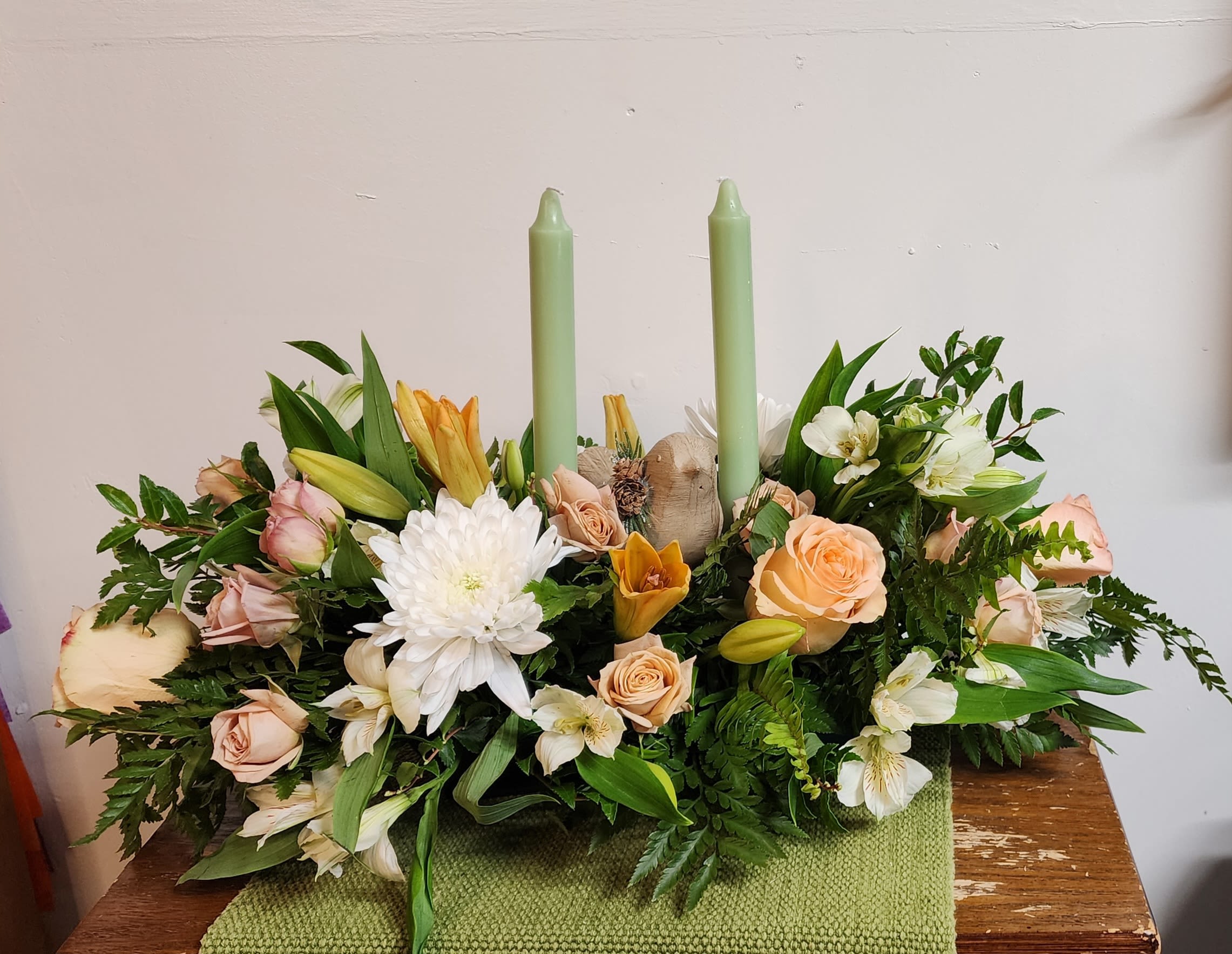 Low floral centerpiece with roses, lilies, and two green candles