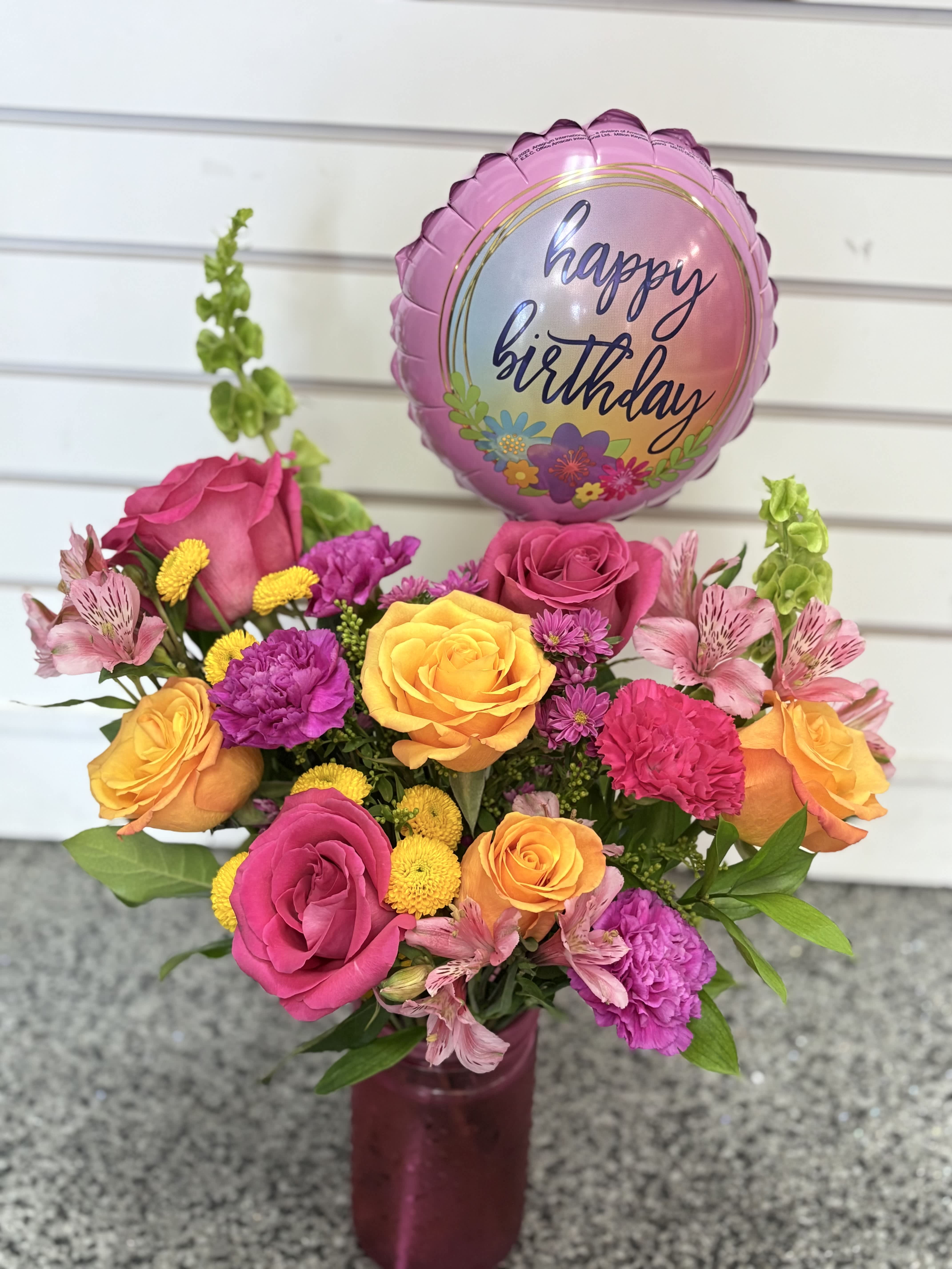 Pink and orange rose bouquet with a happy birthday balloon in a vase