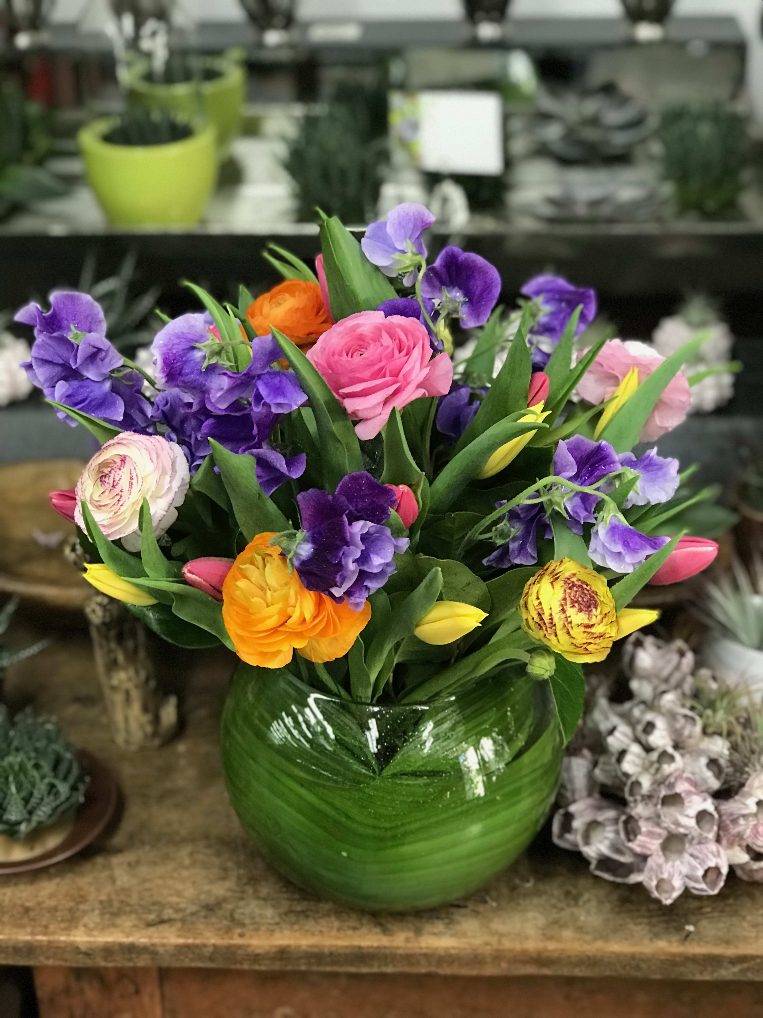 Colorful bouquet of pink, purple, yellow, and orange flowers in a green glass vase