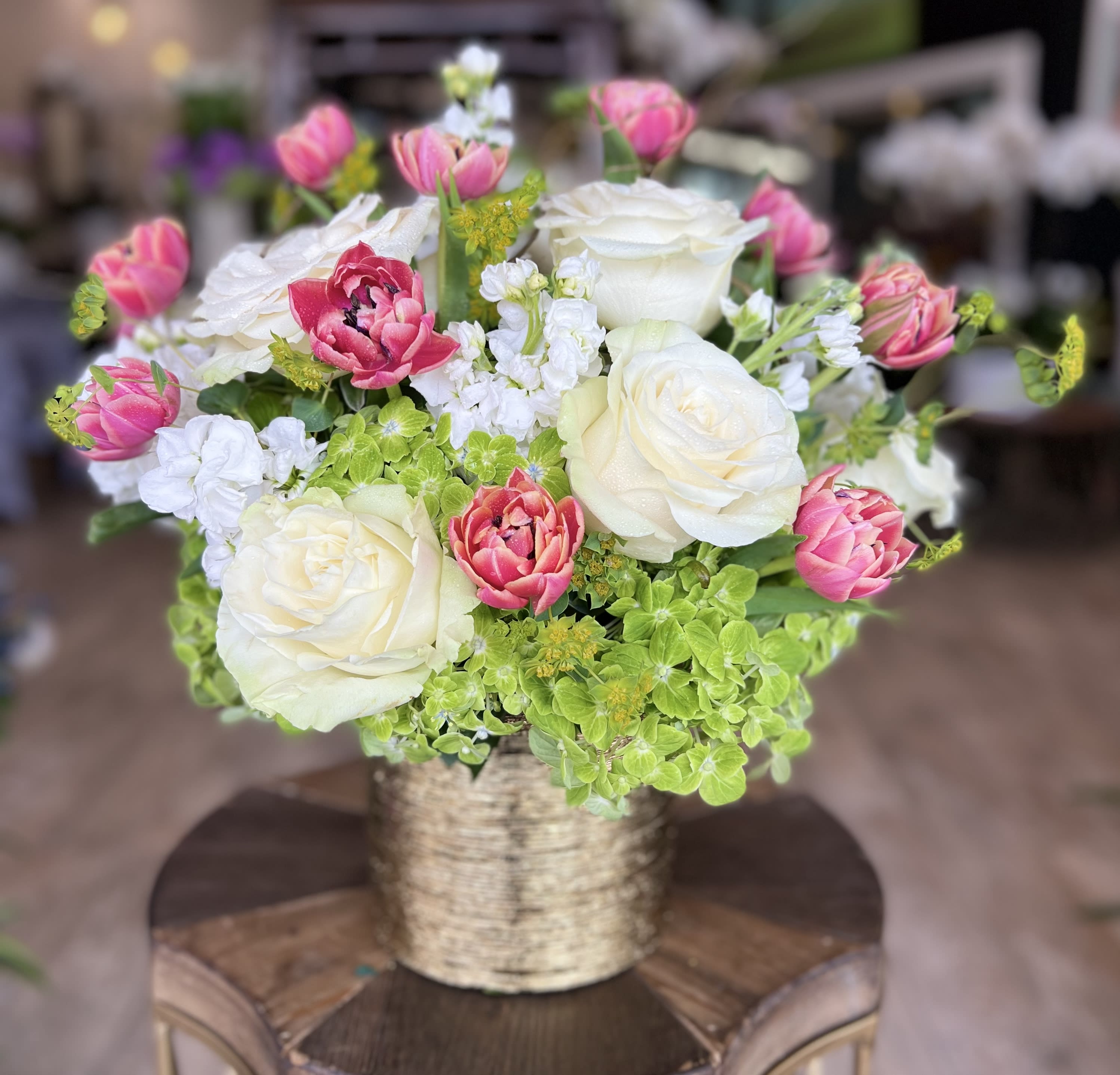 Pink and white roses arranged in a gold vase with green hydrangea accents