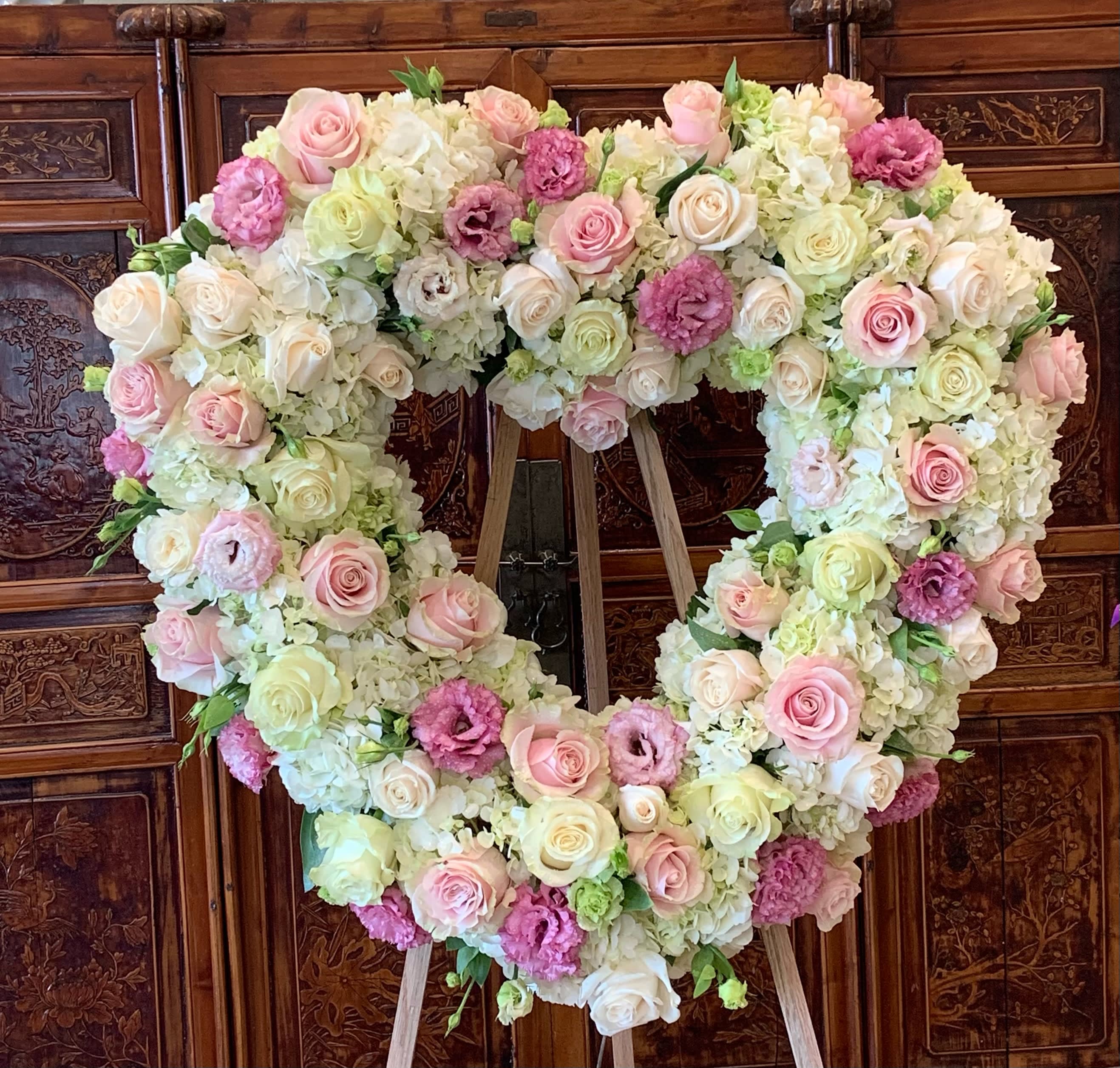 Heart-shaped floral arrangement with pink and white roses on an easel