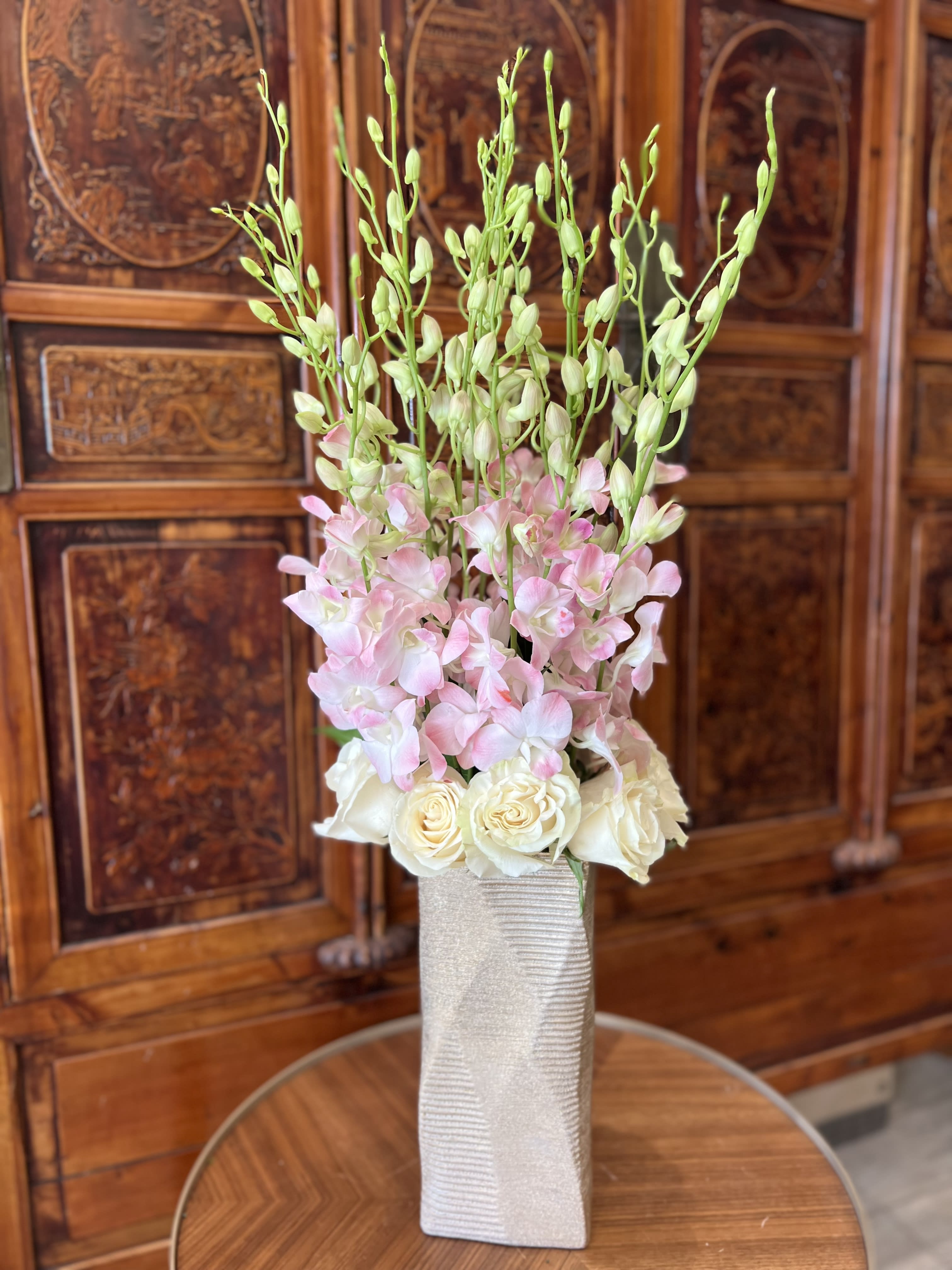 Tall floral arrangement with pink orchids and white roses in a textured vase