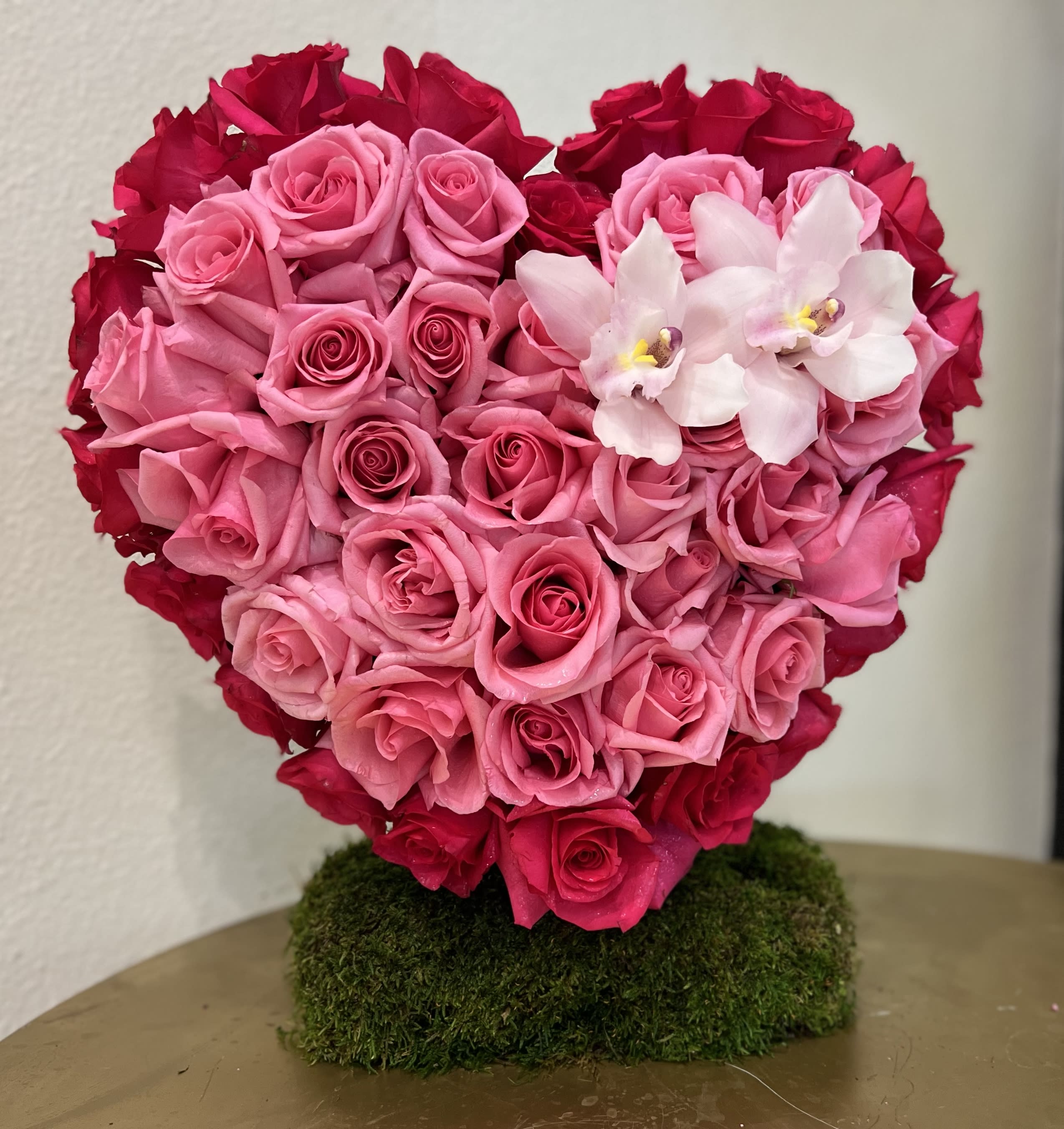 Heart-shaped arrangement of pink and red roses with white orchids on a moss base
