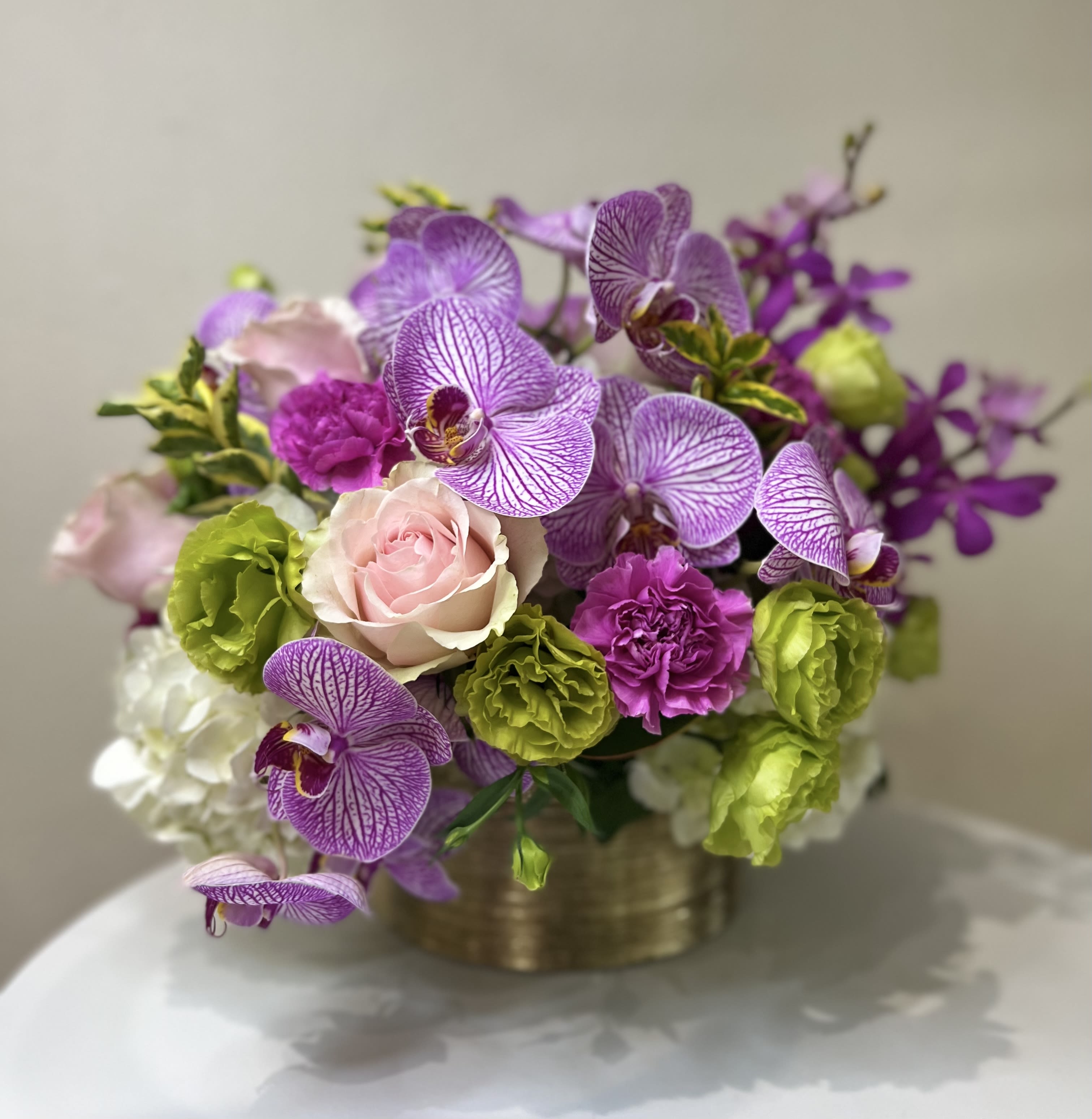 Purple orchids with pink roses and green carnations in a gold container