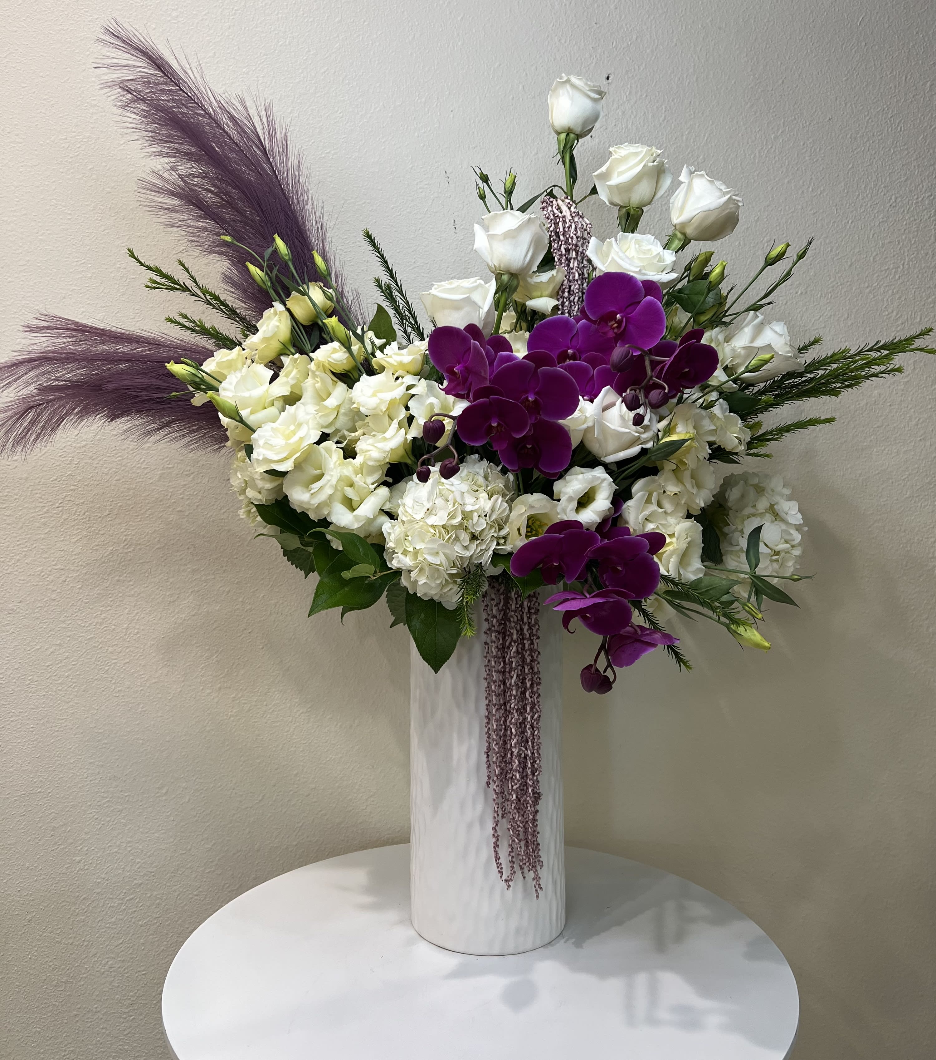 White roses and purple orchids in a tall white vase