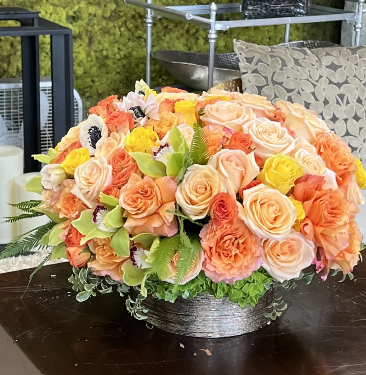 Low floral arrangement of peach, pink, and yellow roses in a silver bowl