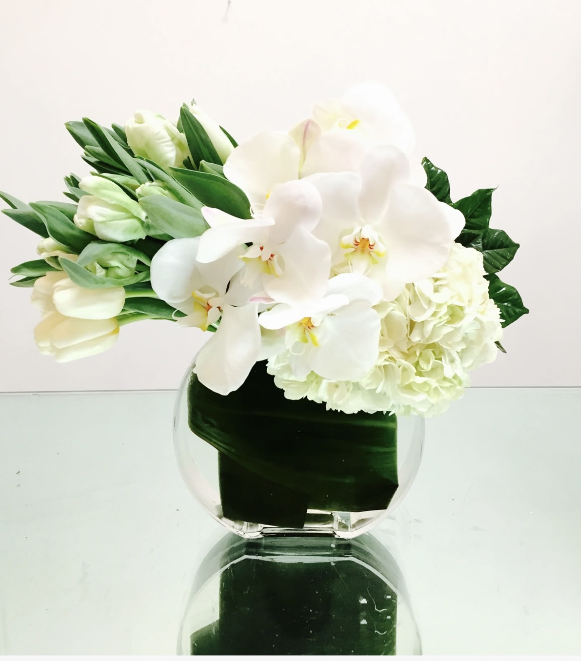 White orchids and pale tulips arranged in a clear glass vase