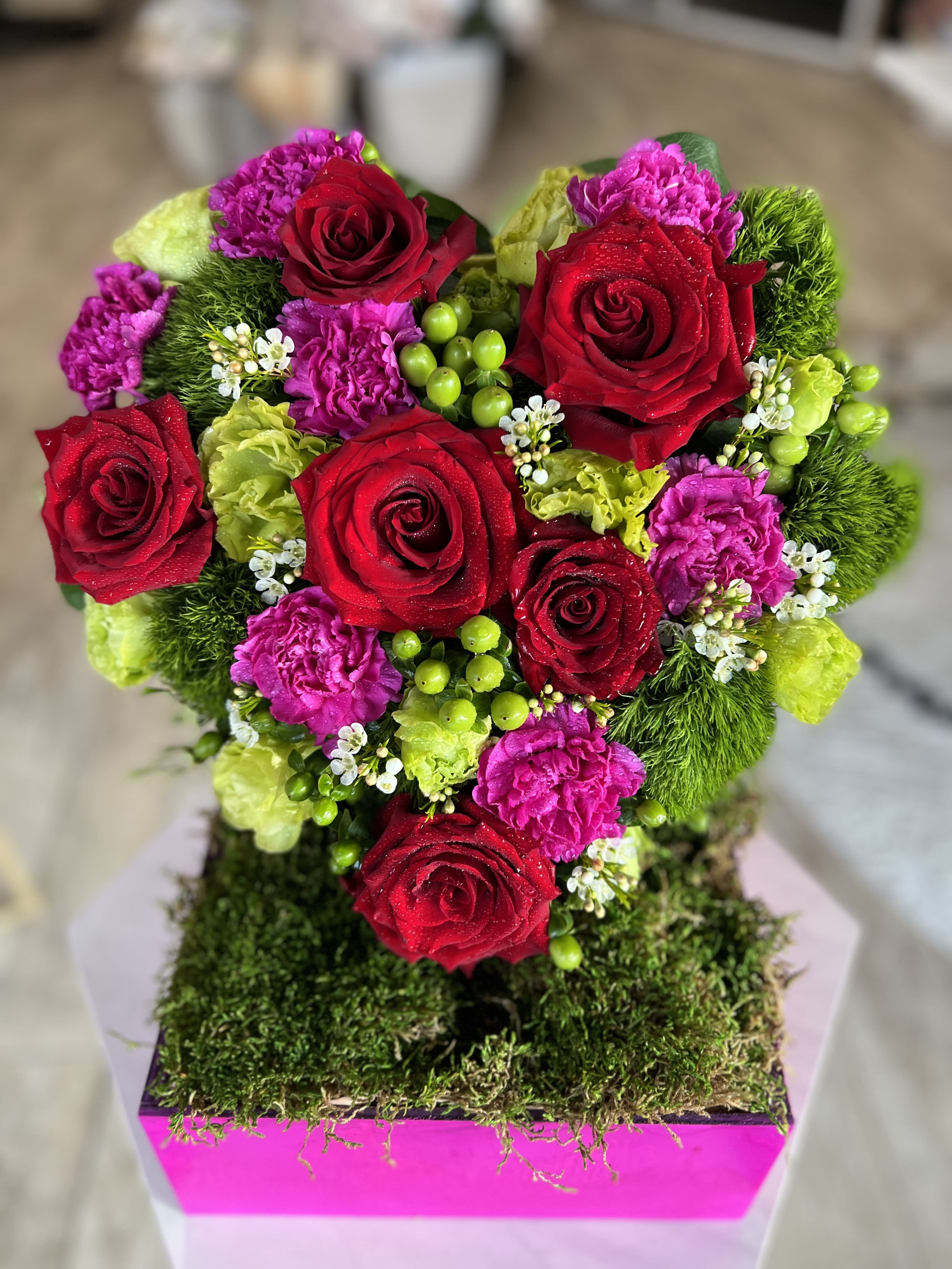 Heart-shaped bouquet of red roses, pink carnations, and green accents