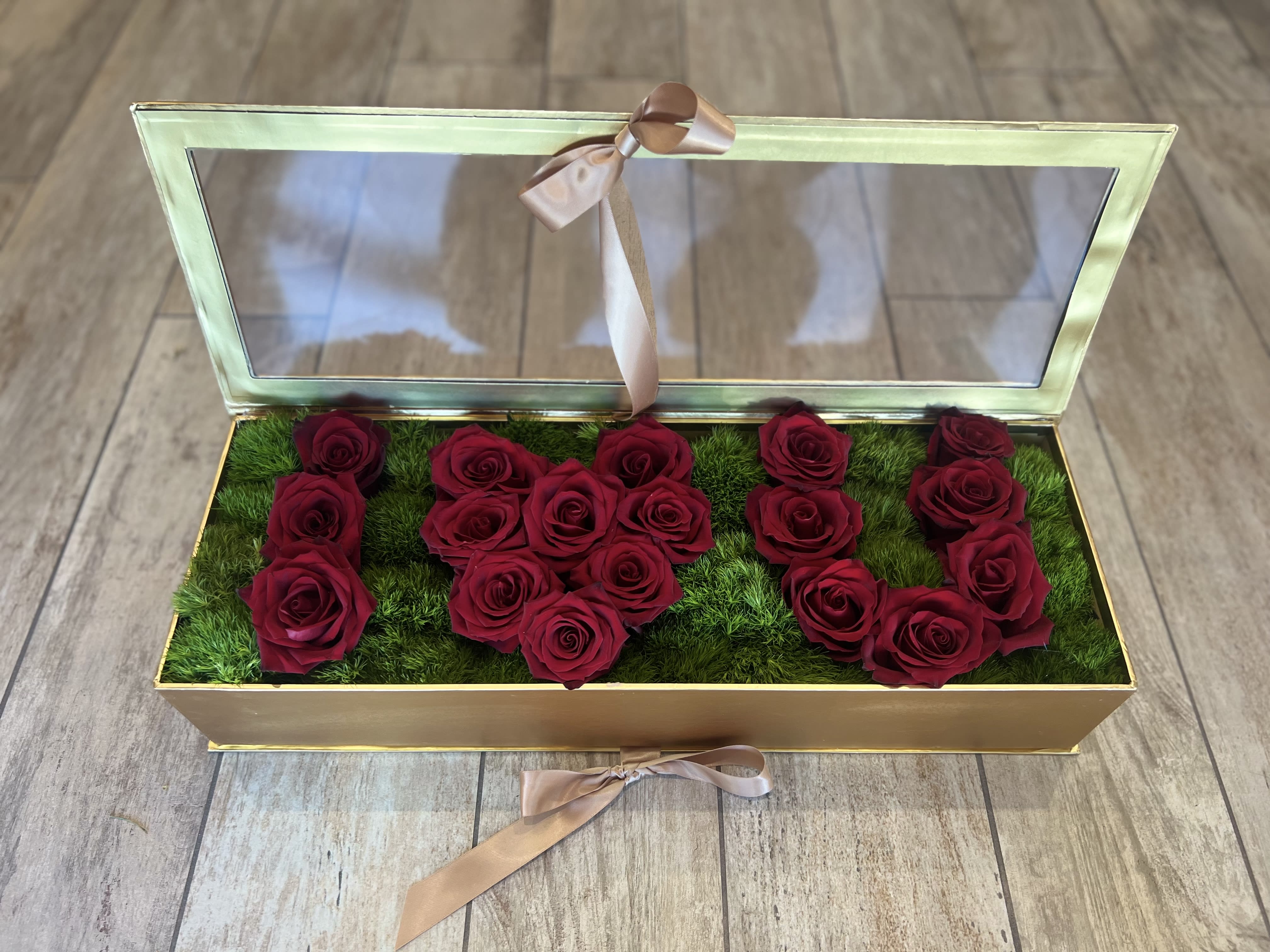 Open gold box with red roses arranged on green moss