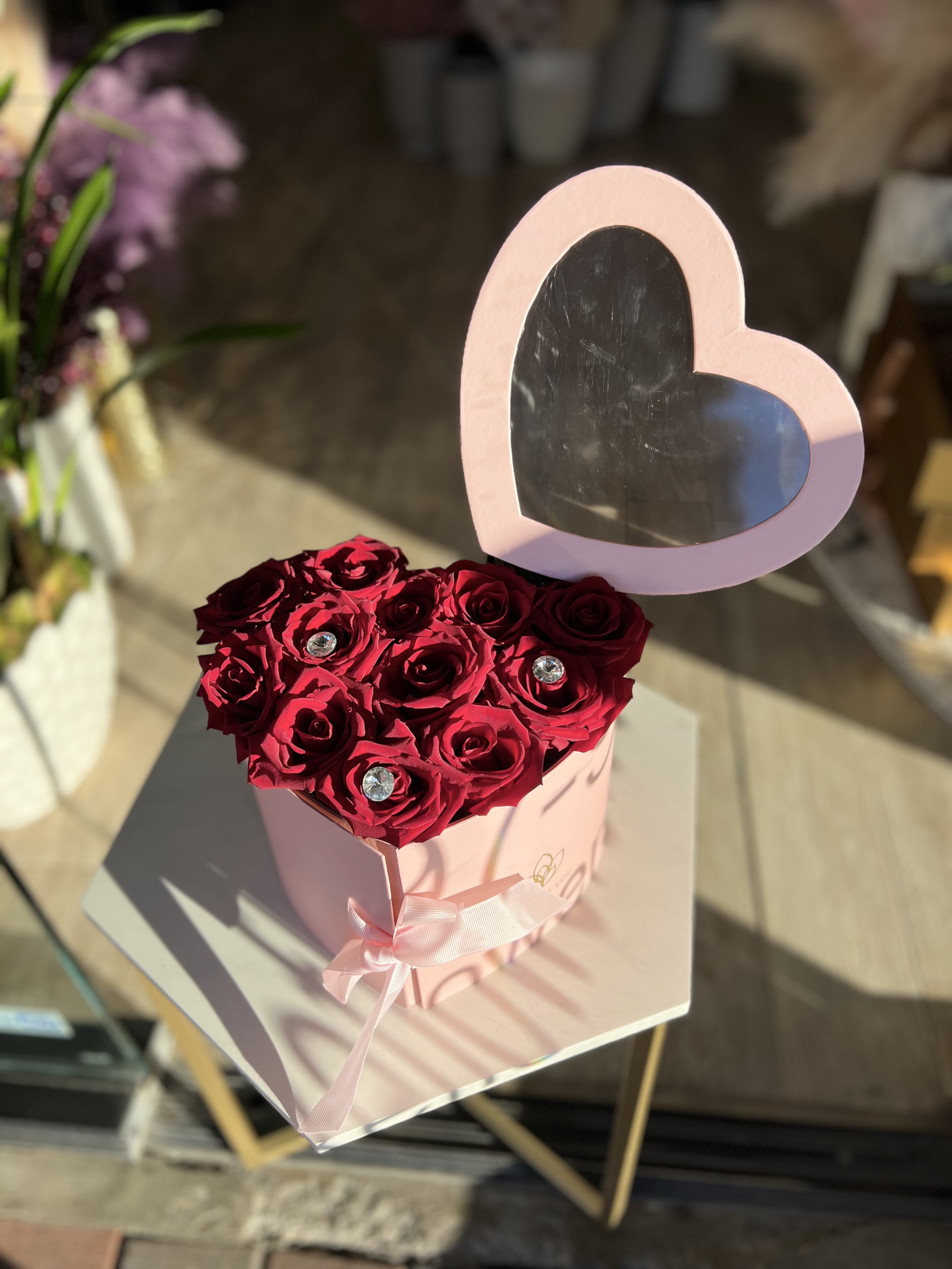 Heart-shaped box of red roses with a pink heart topper