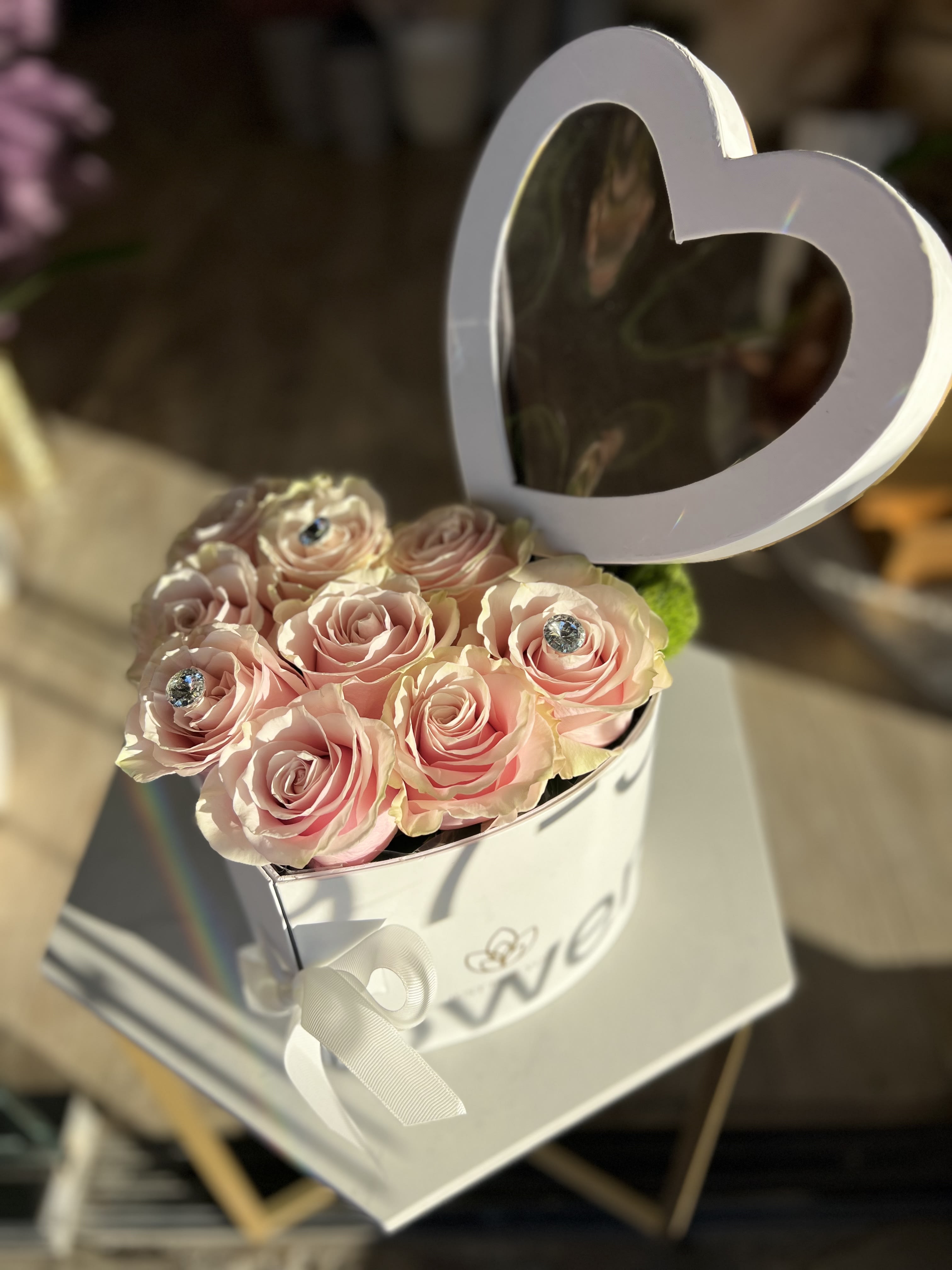 Pink roses in a white heart-shaped box with a ribbon bow