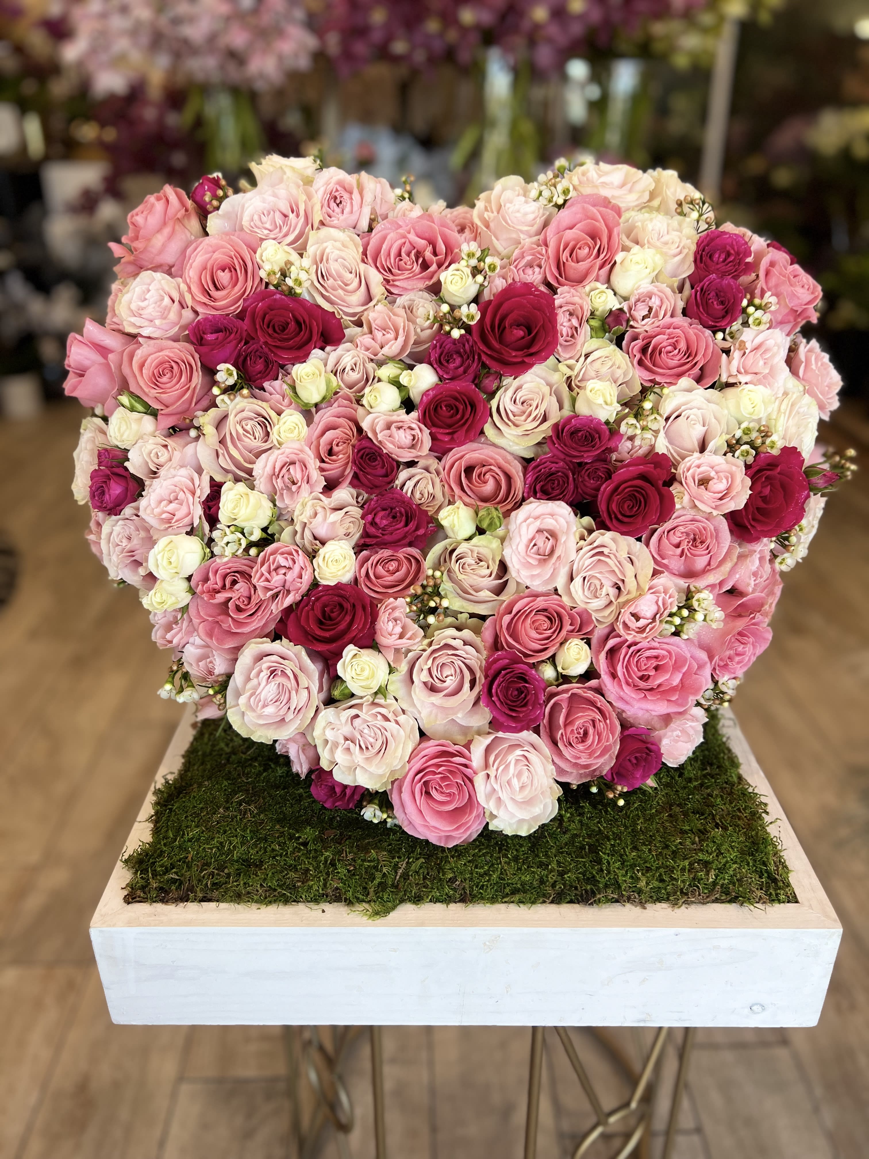 Heart-shaped arrangement of pink and white roses on a moss-covered base