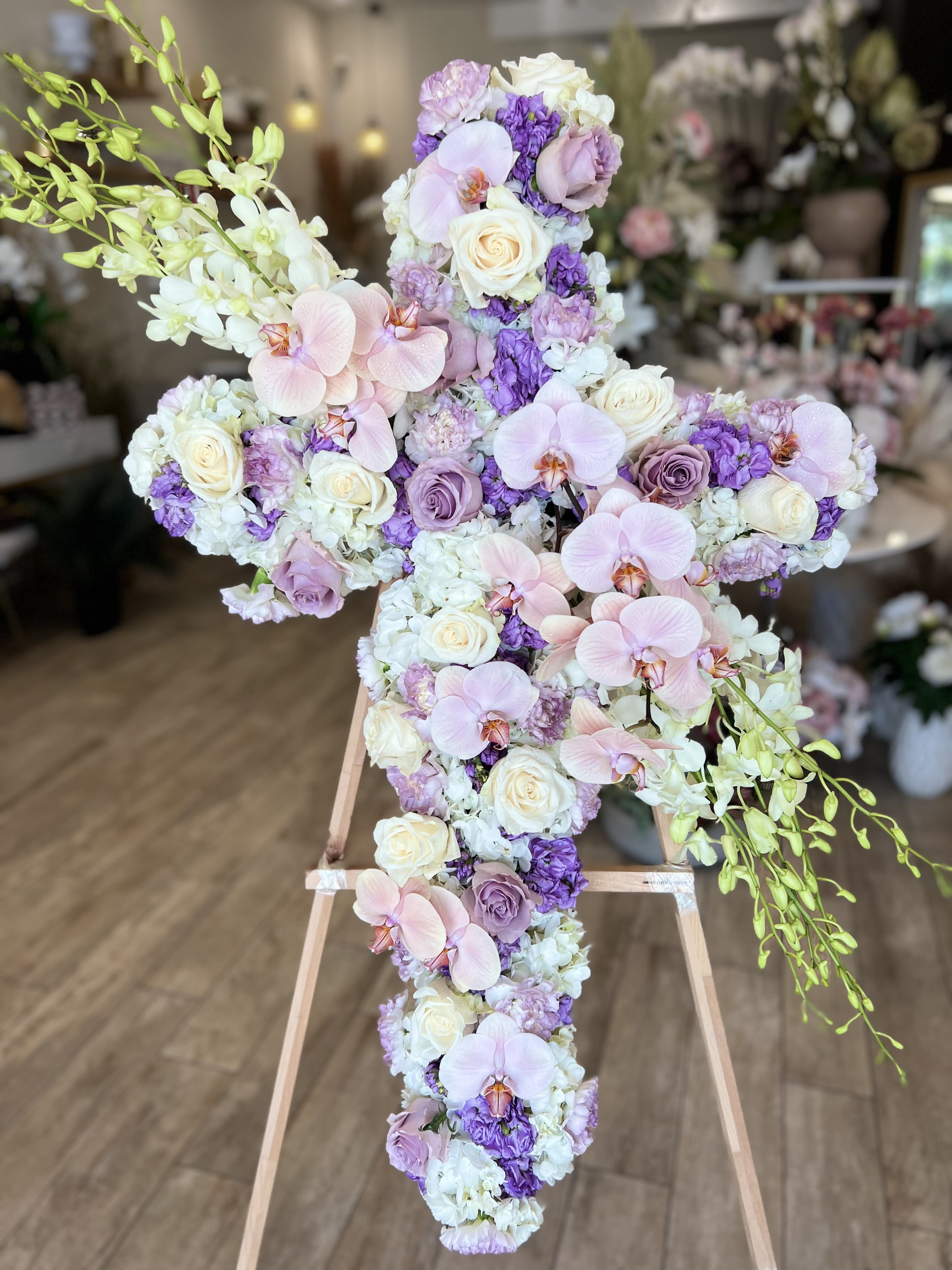 Cross-shaped floral arrangement with pink orchids, white roses, and purple blooms