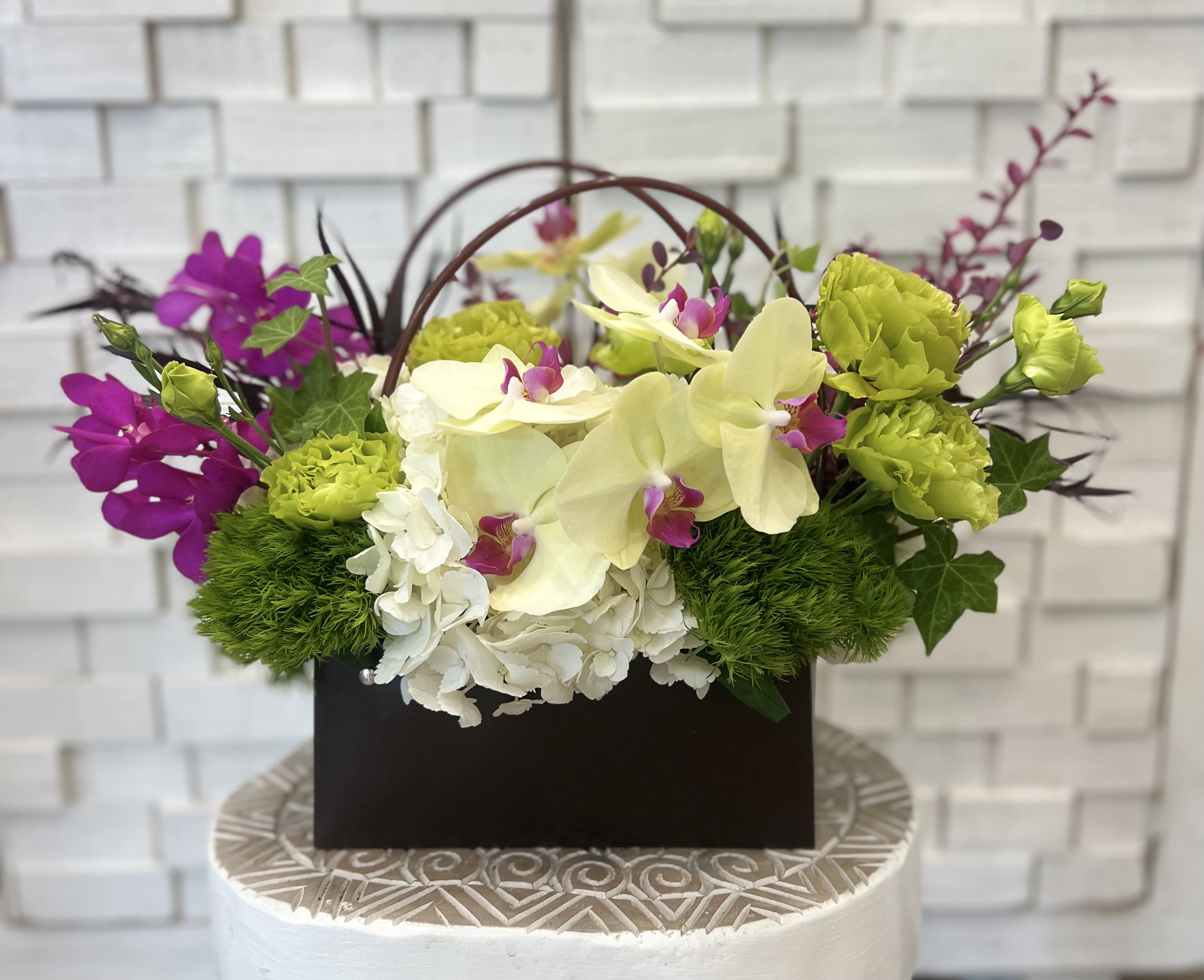 Floral arrangement with orchids, hydrangeas, and green carnations in a dark box