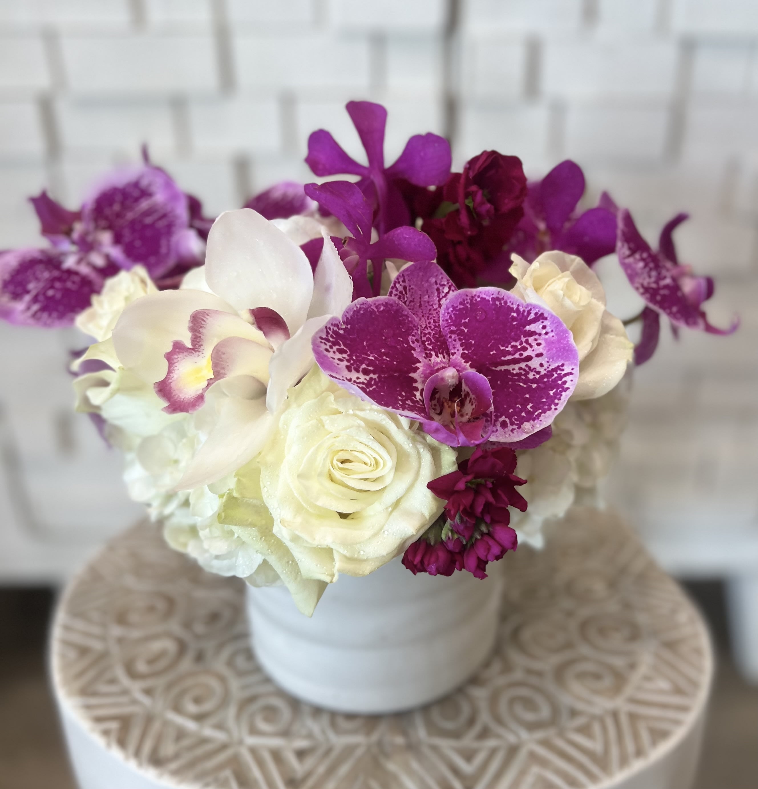 White roses and purple orchids arranged in a white vase